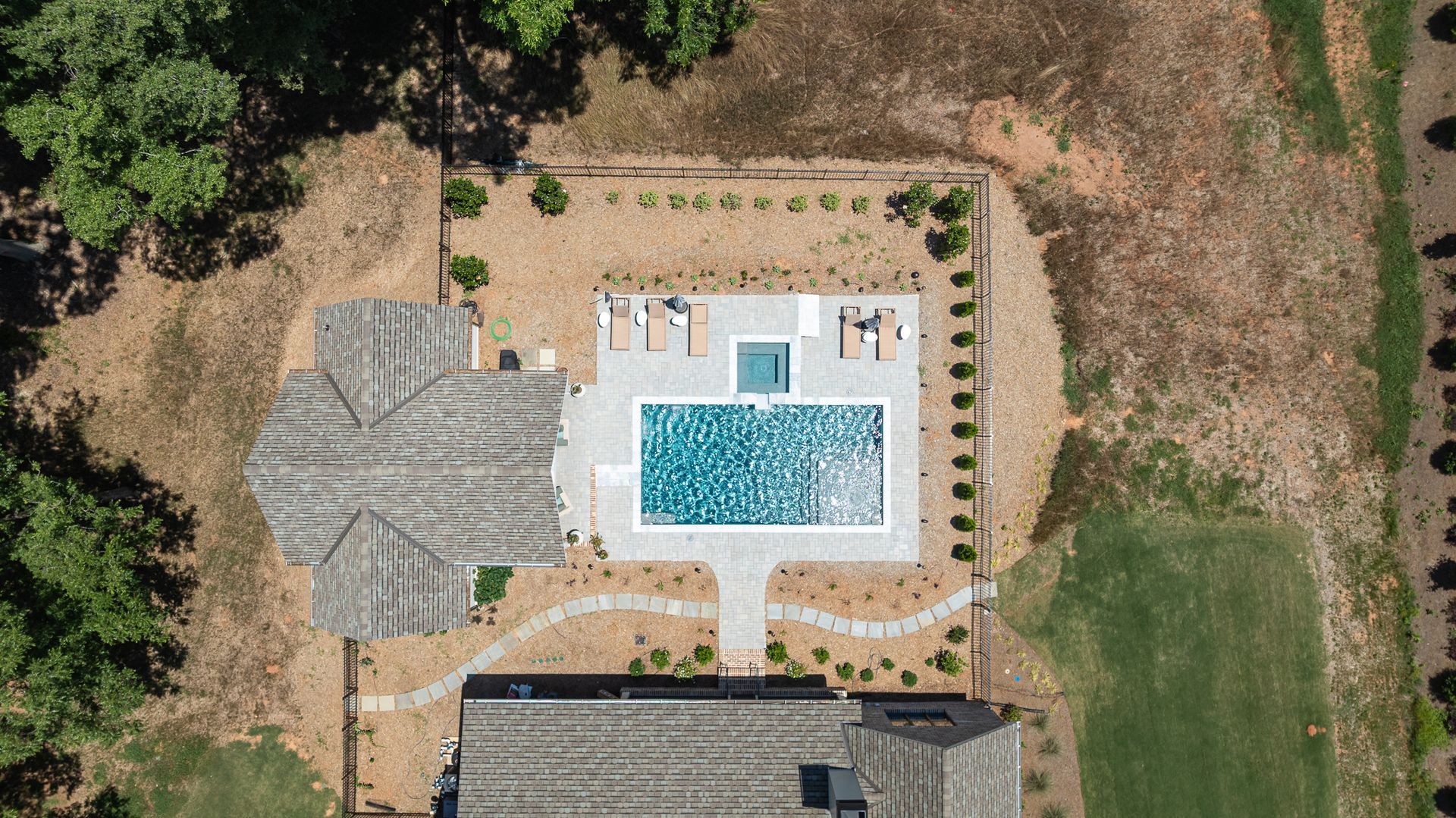 Aerial view of a backyard with a rectangular swimming pool, lounge chairs, and surrounding dry landscaping.