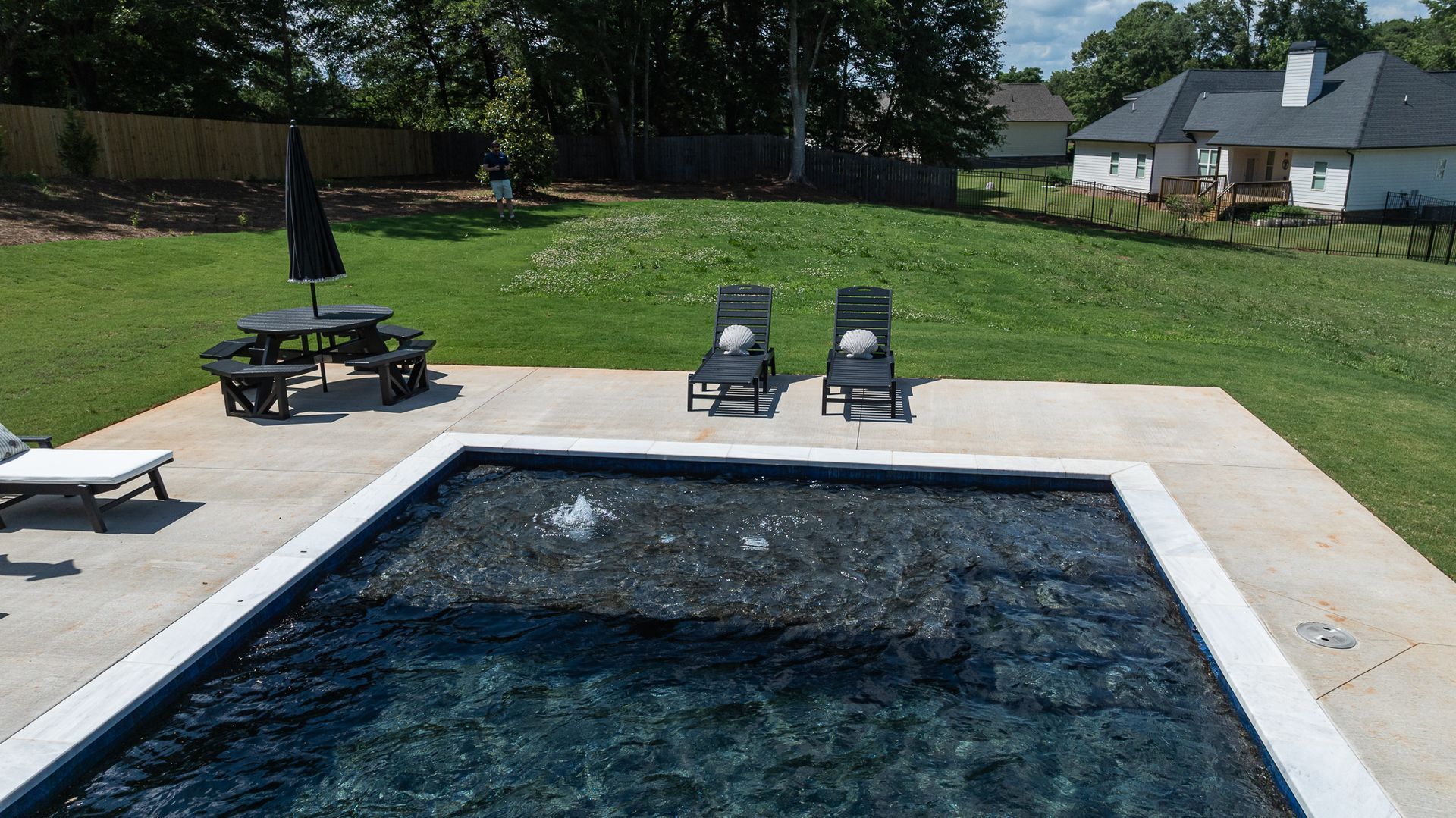 Backyard swimming pool with two lounge chairs and a picnic table on a sunny lawn