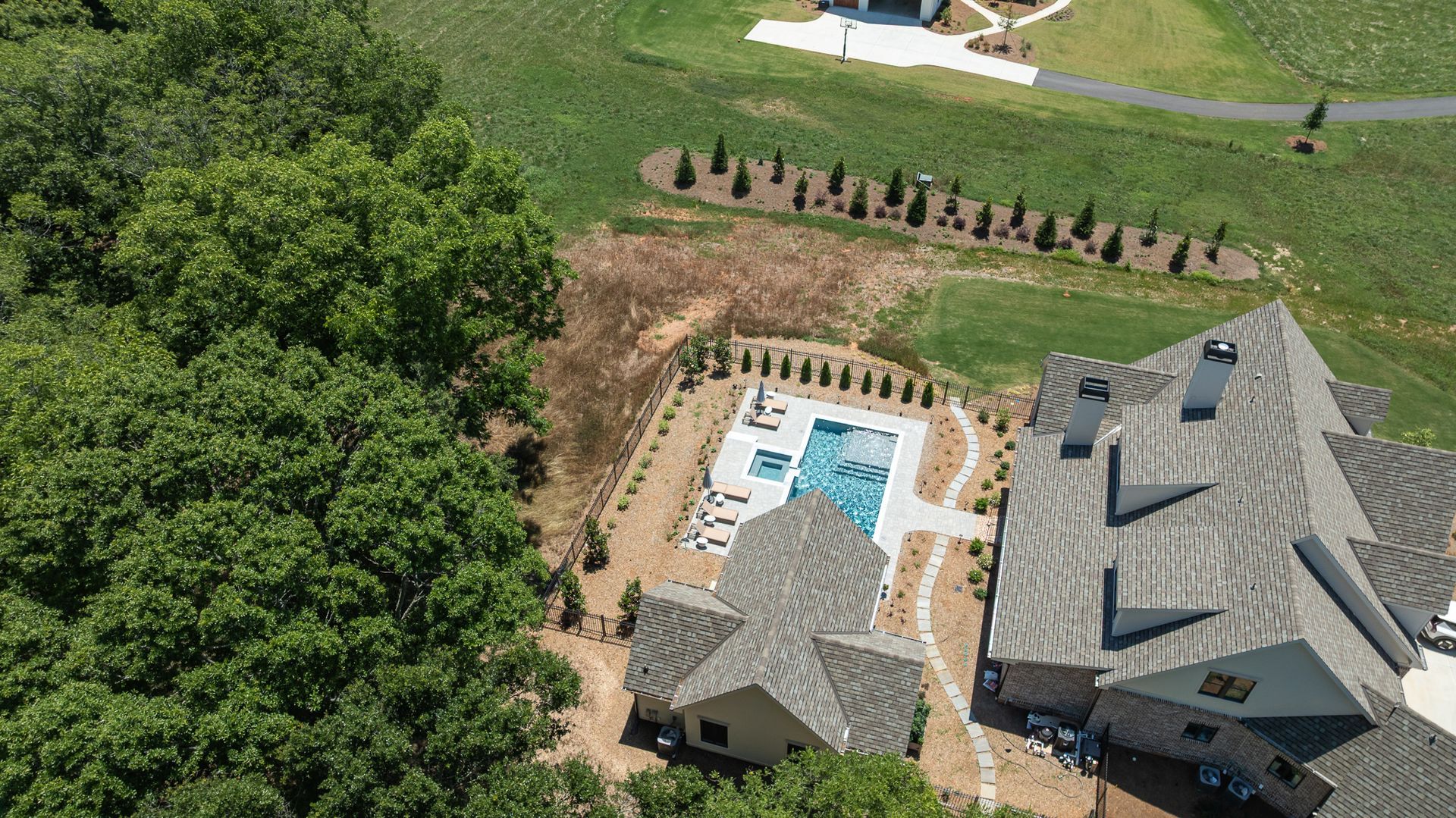 Aerial view of a house with a backyard pool, patio, and surrounding trees and lawn.
