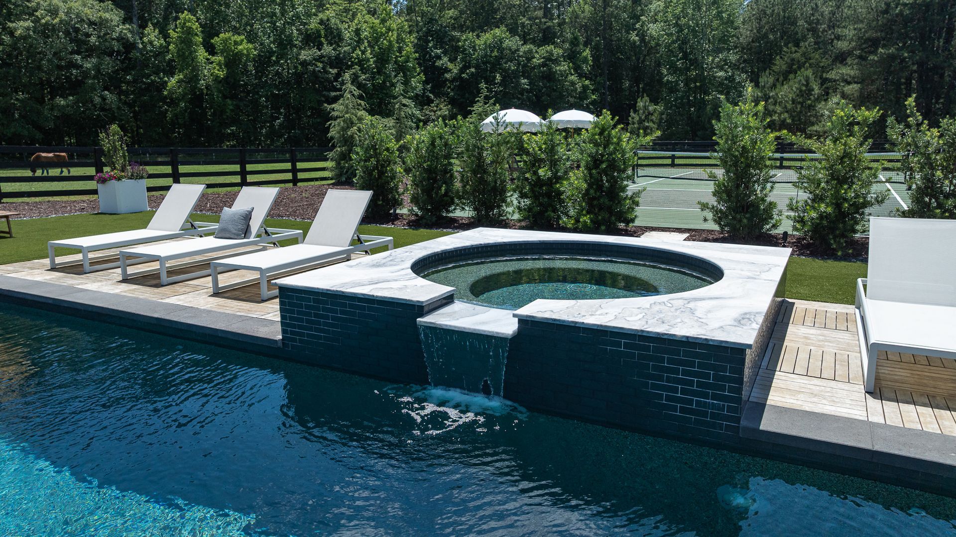 Backyard pool with a raised hot tub, white lounge chairs, and green trees in the background
