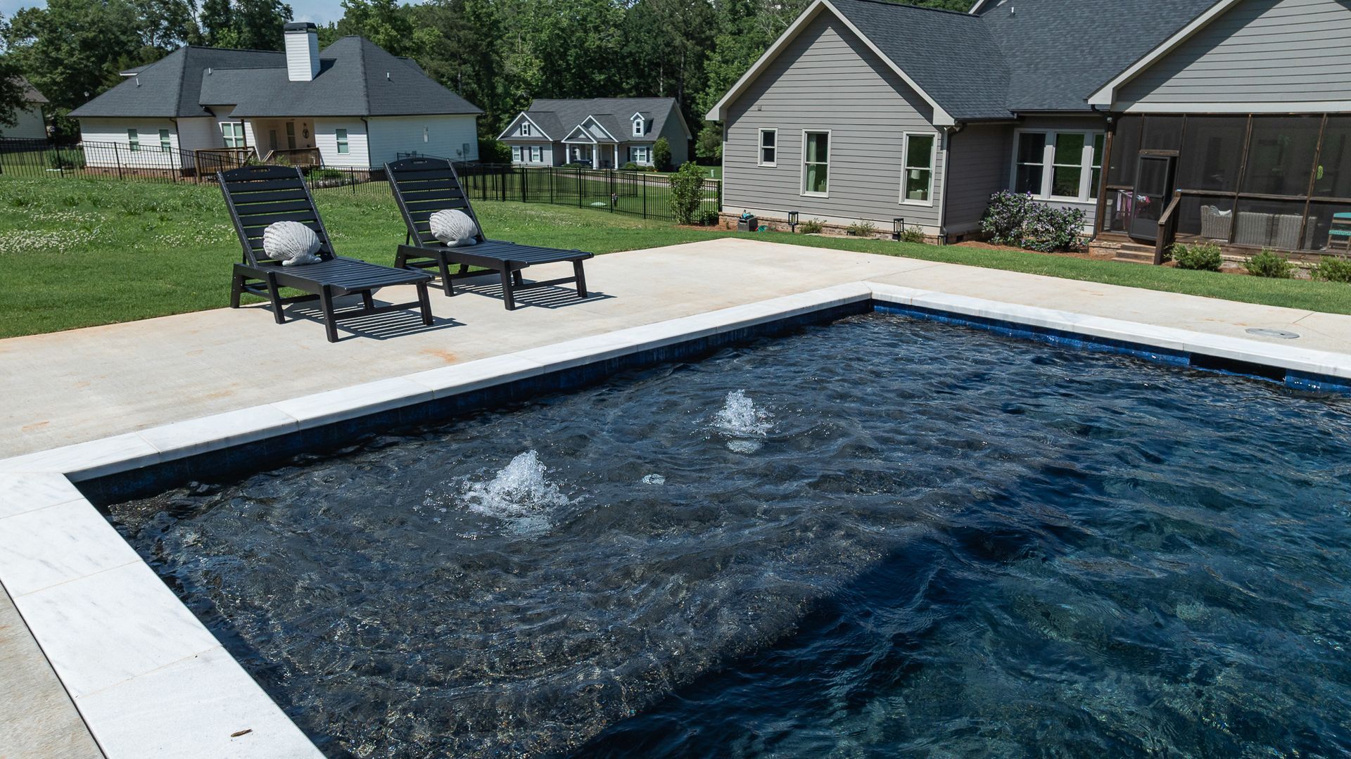 Backyard pool with dark water, bubbling jets, and lounge chairs beside a house