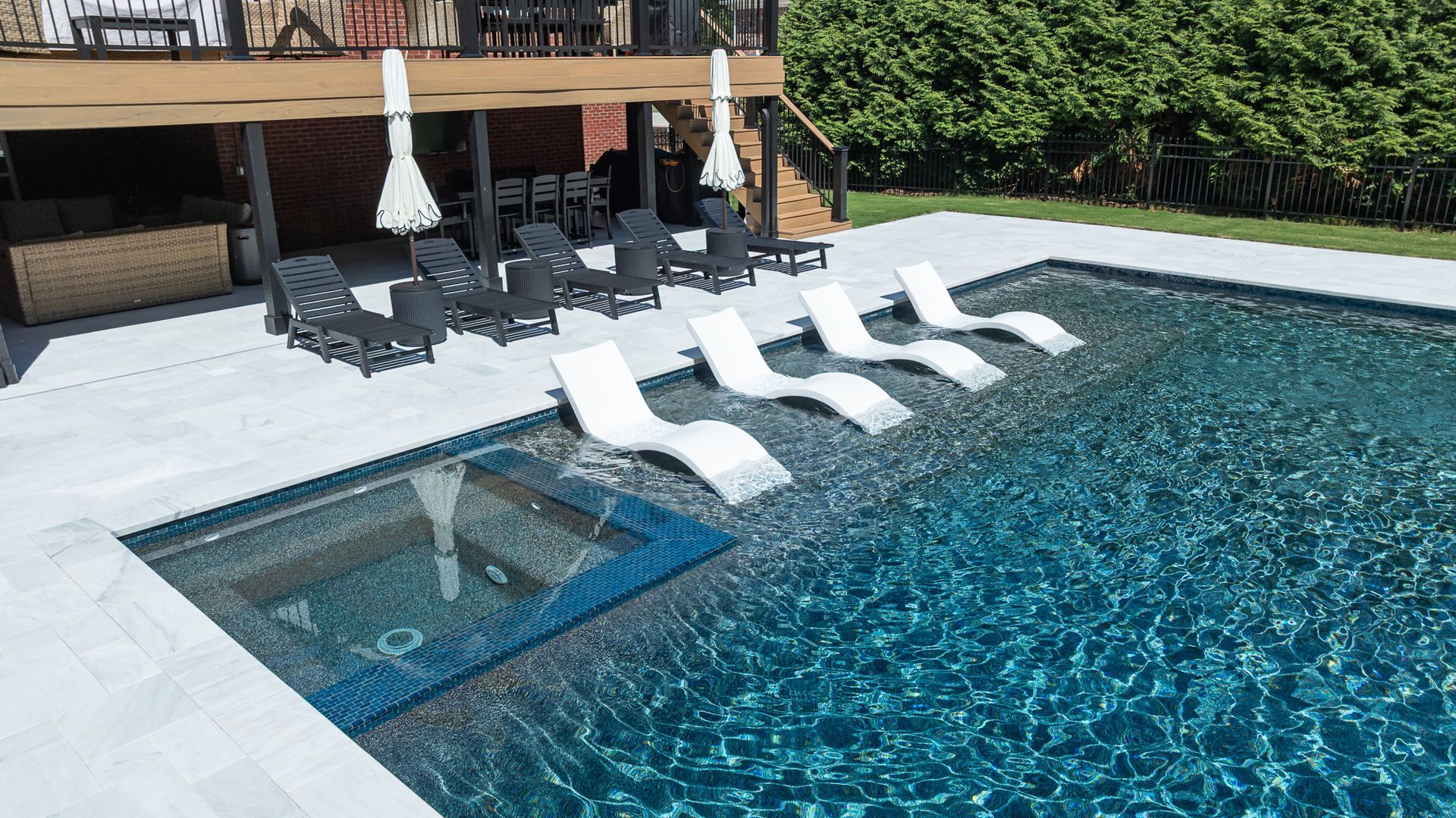 Modern pool deck with four white lounge chairs and a small hot tub beside turquoise water