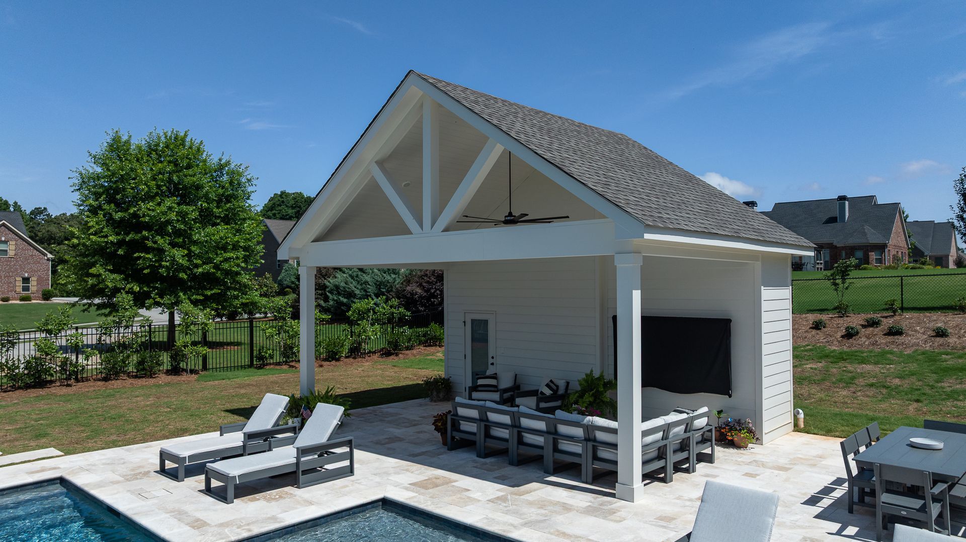 Modern white poolside pavilion with gray lounge chairs and a covered seating area in a sunny yard