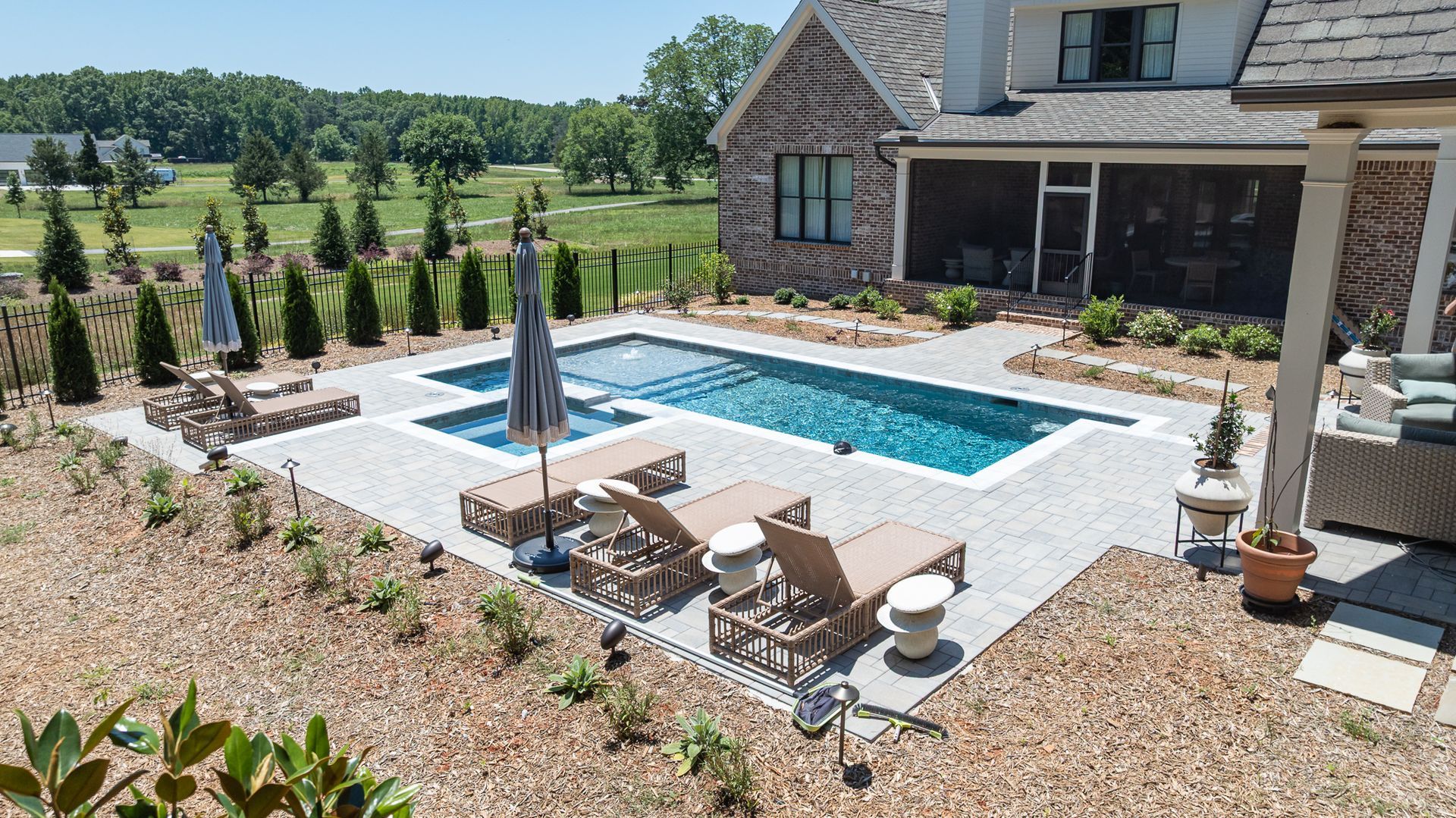 Backyard patio with a rectangular pool, lounge chairs, umbrella, and stone house in the background