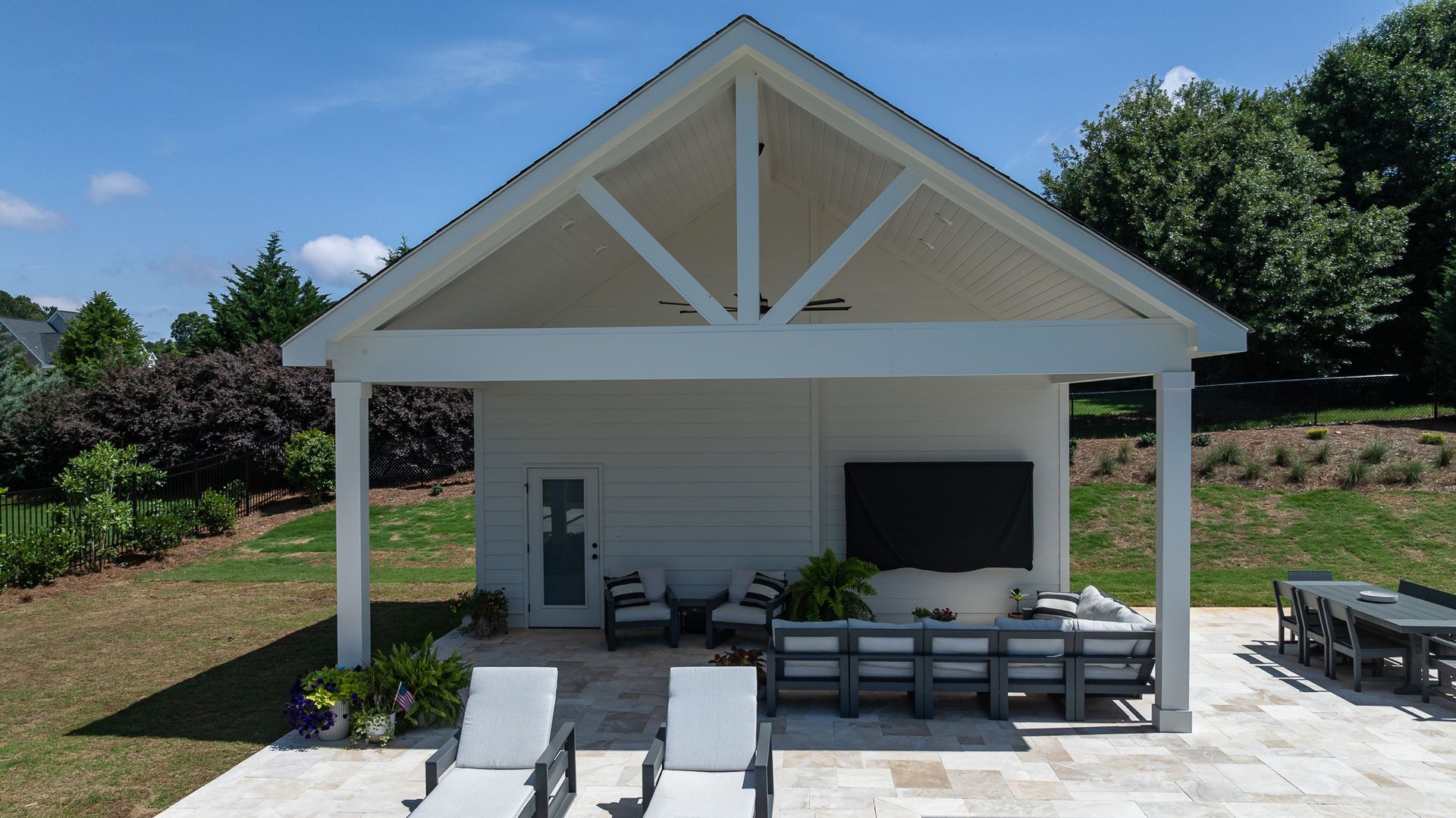 White patio cabana with lounge chairs and sofa seating on a sunny backyard terrace.