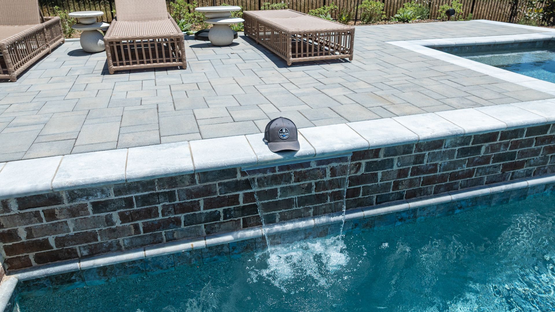 Poolside lounge chairs beside a raised brick spa with water spilling into the pool