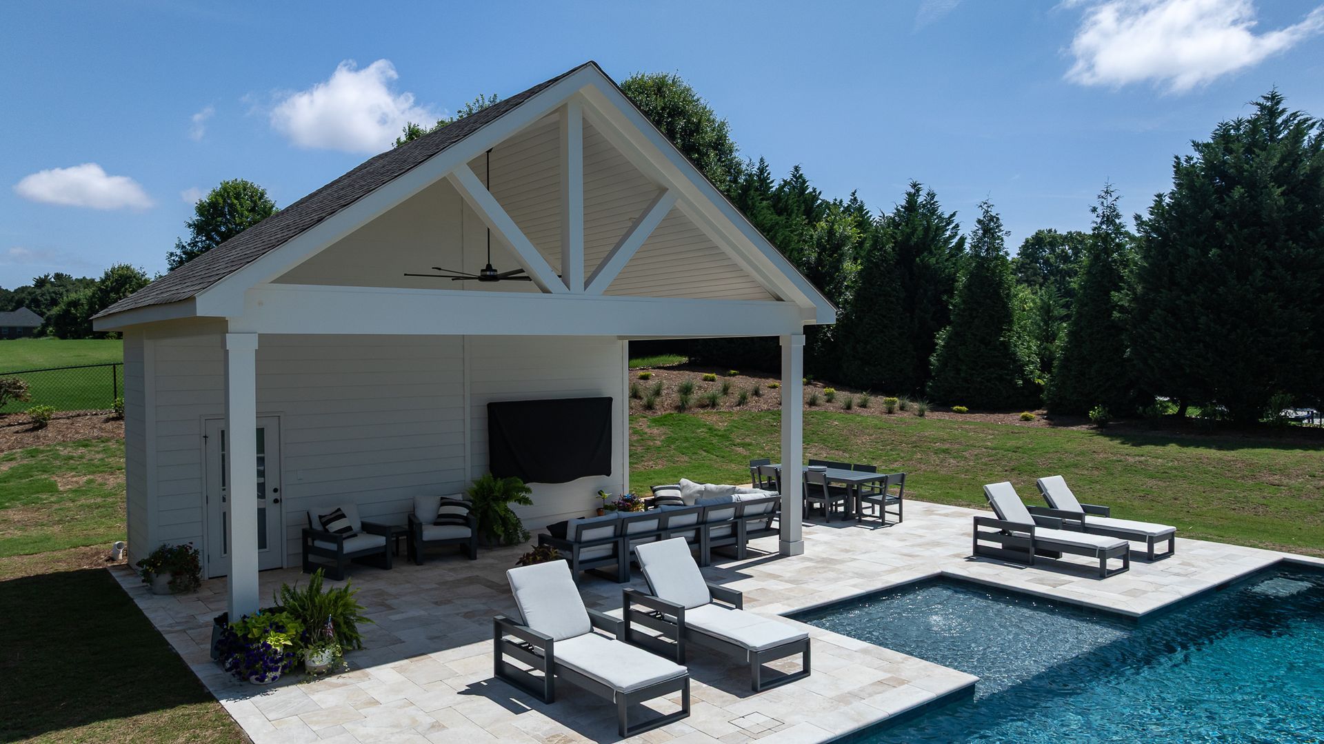 Modern backyard pool with white cabana, lounge chairs, and sunny blue sky