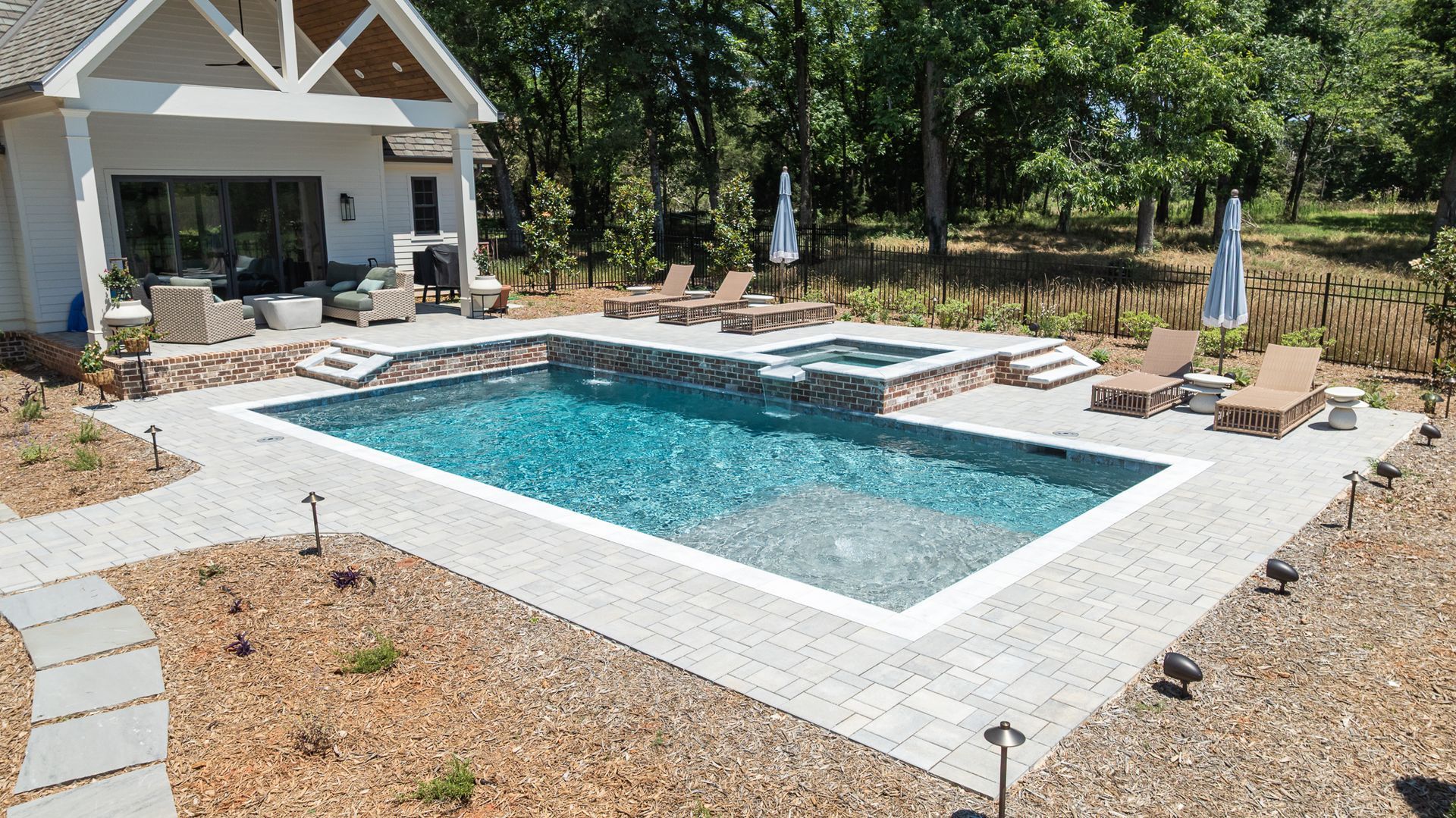 Backyard pool with turquoise water, spa, lounge chairs, and a covered patio surrounded by trees