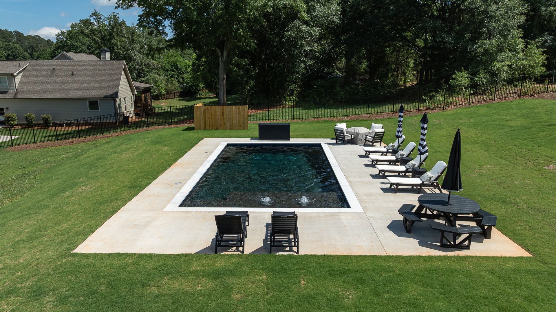 Backyard pool with lounge chairs on a concrete patio, surrounded by green lawn and trees