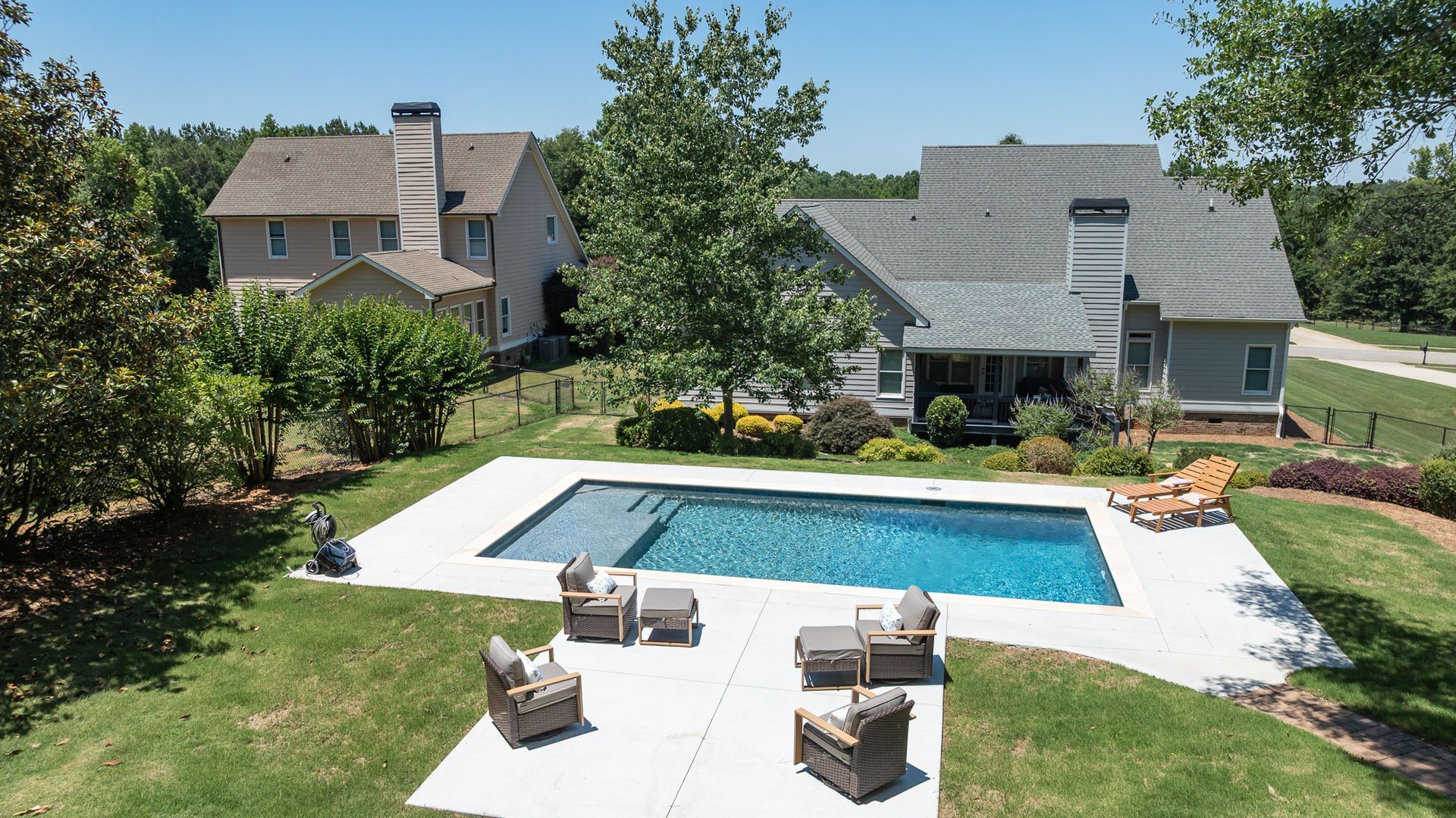 Backyard patio with a rectangular swimming pool, lounge chairs, and houses in the background.