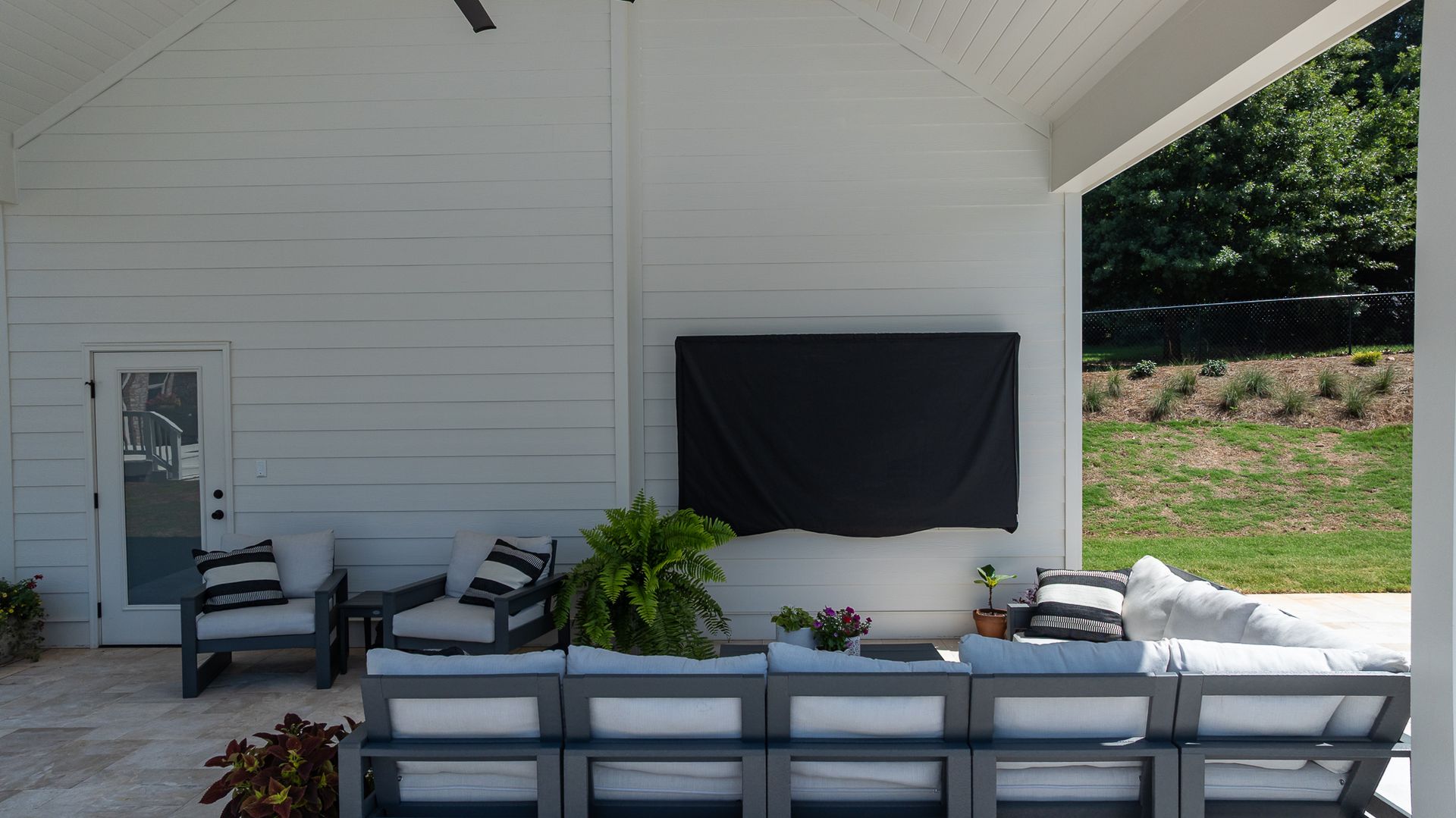 Covered patio with white outdoor seating, black wall art, and a green lawn view beyond.