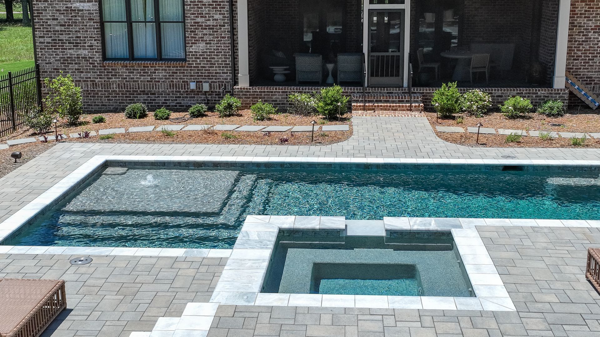 Backyard pool with a square hot tub and tiled coping beside a brick patio and house façade