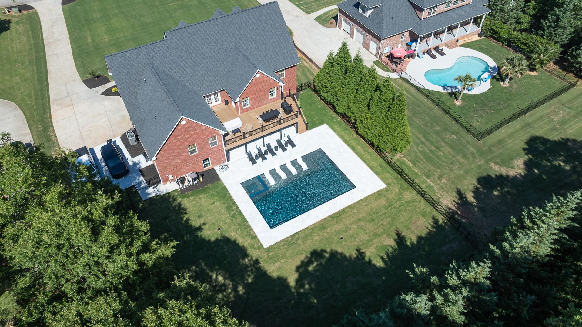 Aerial view of a house with a backyard pool, patio, and surrounding lawn.