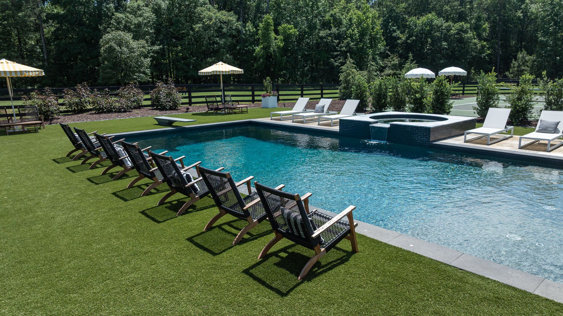 Poolside lounge chairs beside a blue resort pool with green lawn and trees in the background