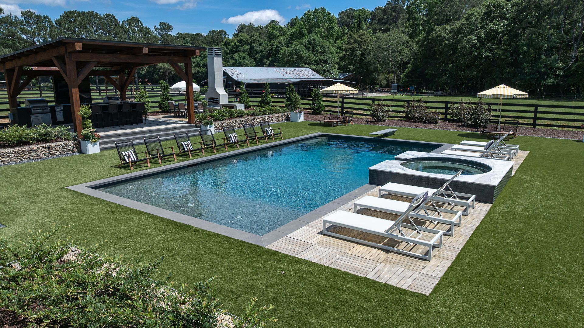 Backyard swimming pool with lounge chairs, covered patio, and green lawn on a sunny day