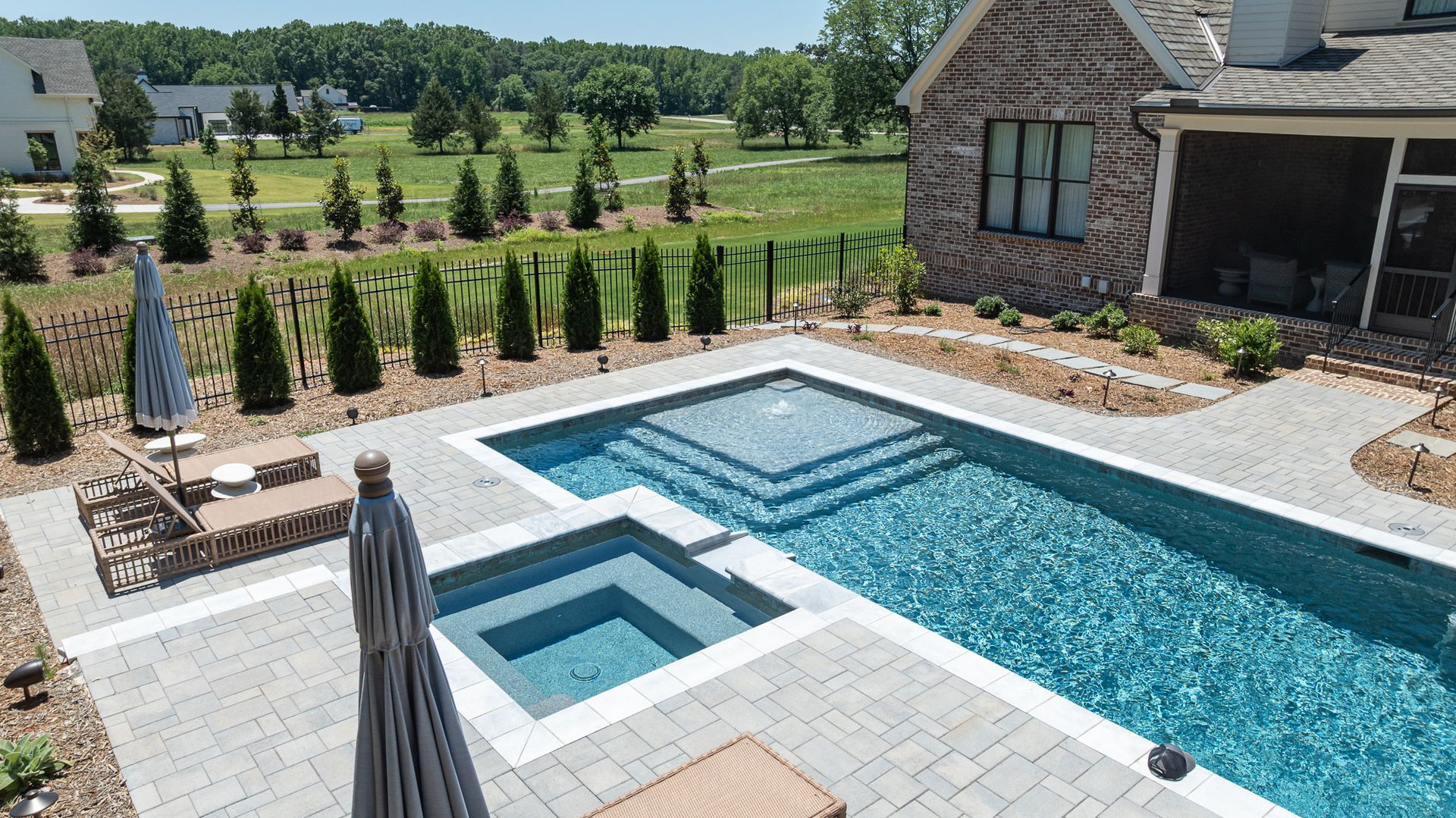 Backyard pool with raised spa, stone patio, lounge chairs, and landscaped lawn beside a house