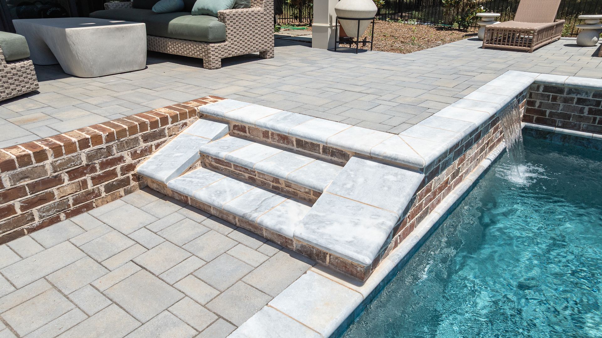 Poolside stone steps and deck beside a swimming pool with outdoor seating.