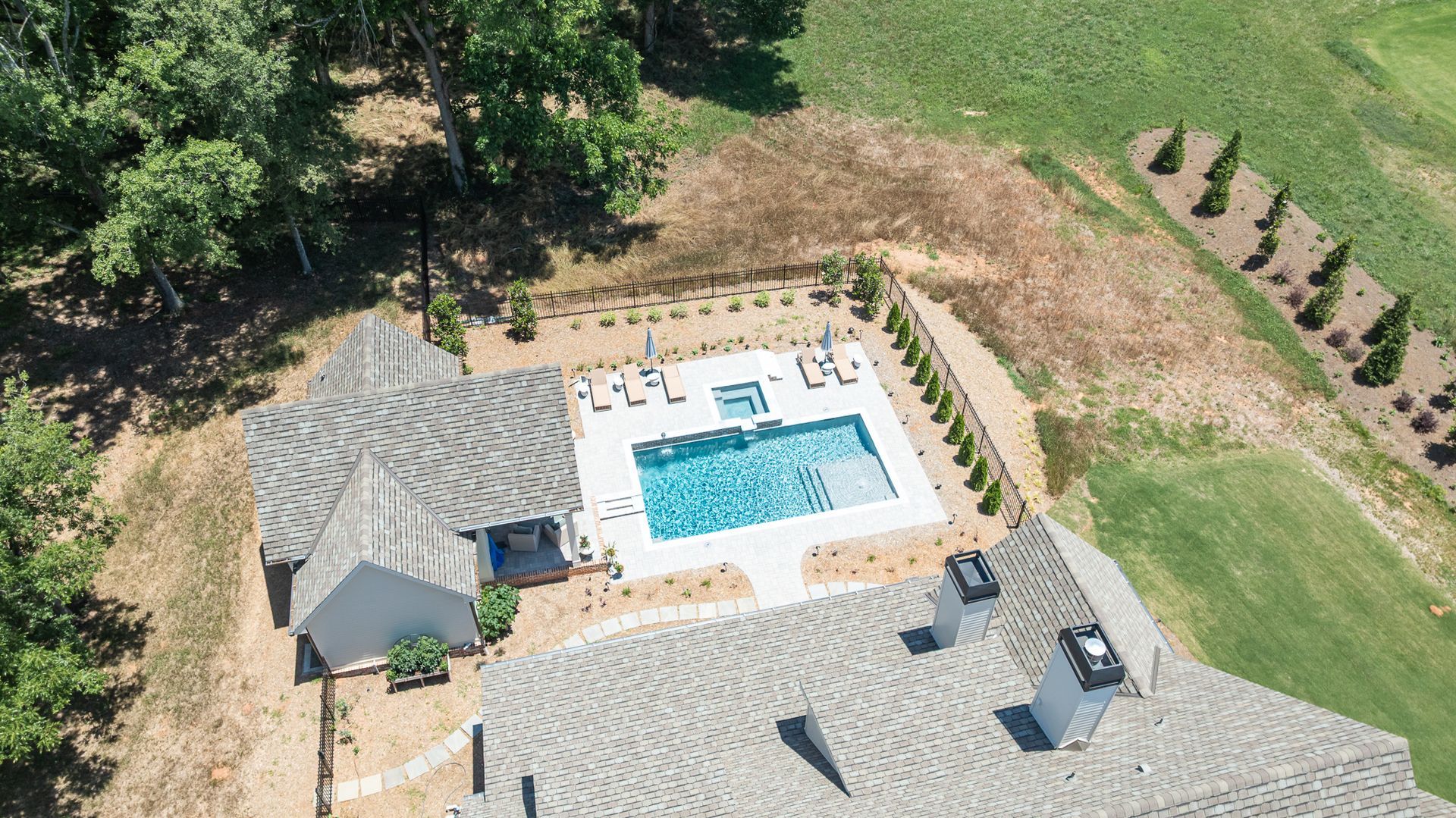 Aerial view of a backyard with a swimming pool, patio furniture, and a house roof nearby.