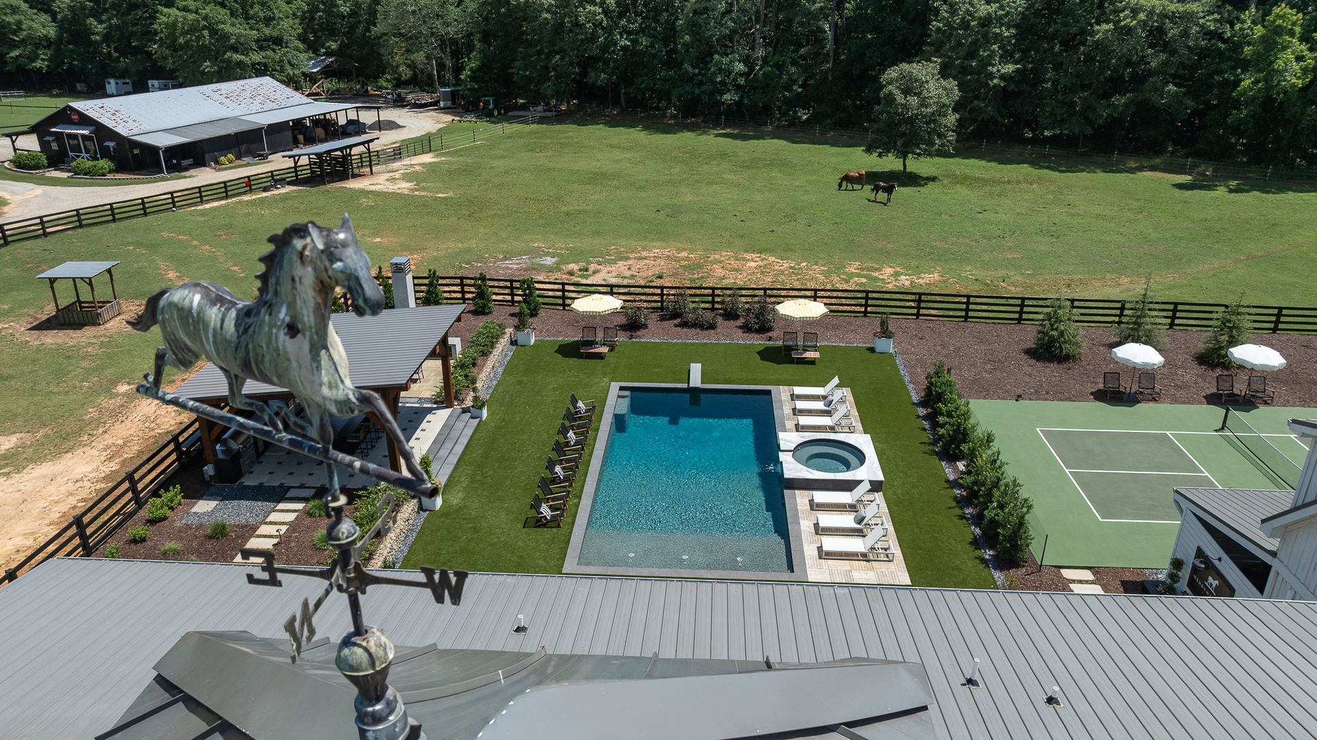 Aerial view of a backyard with a swimming pool, patio furniture, and a large metal sculpture on the lawn.