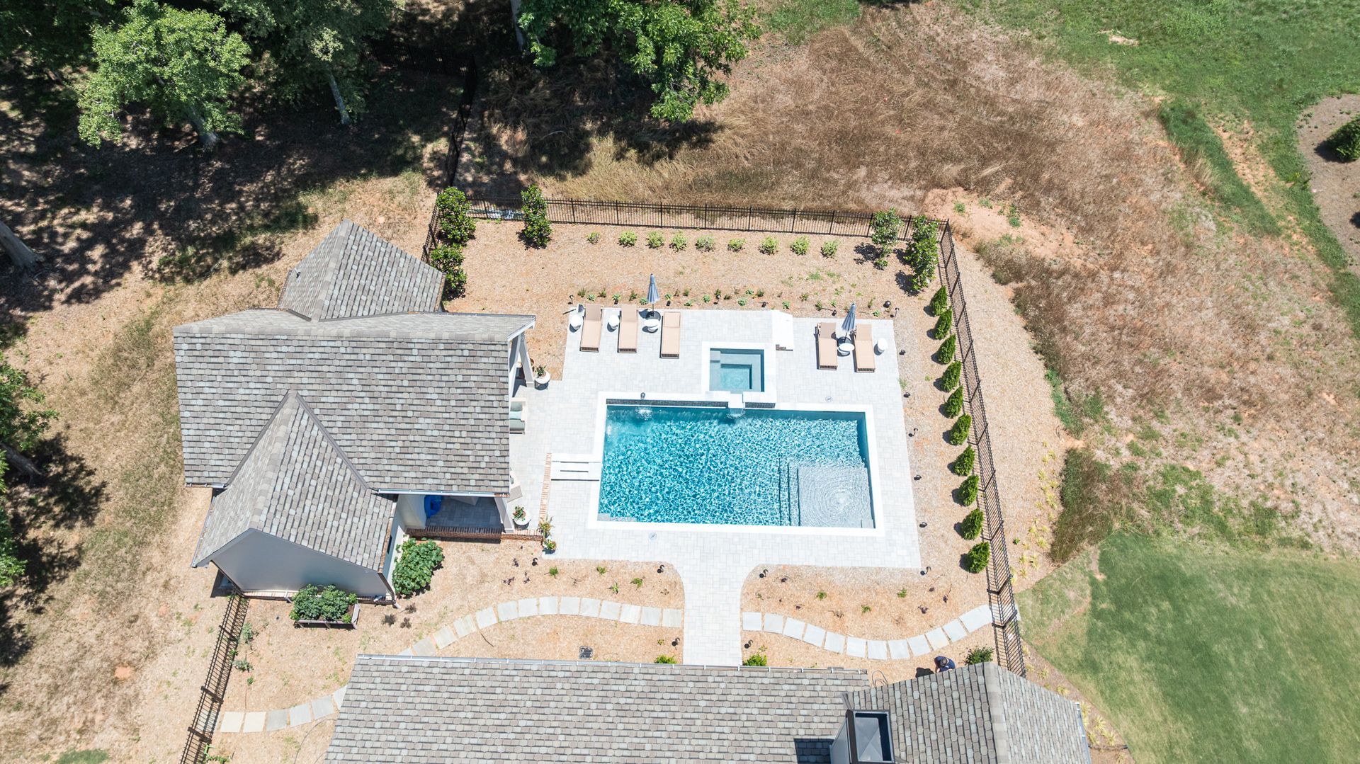 Aerial view of a backyard patio with a swimming pool, lounge chairs, and surrounding trees and lawn