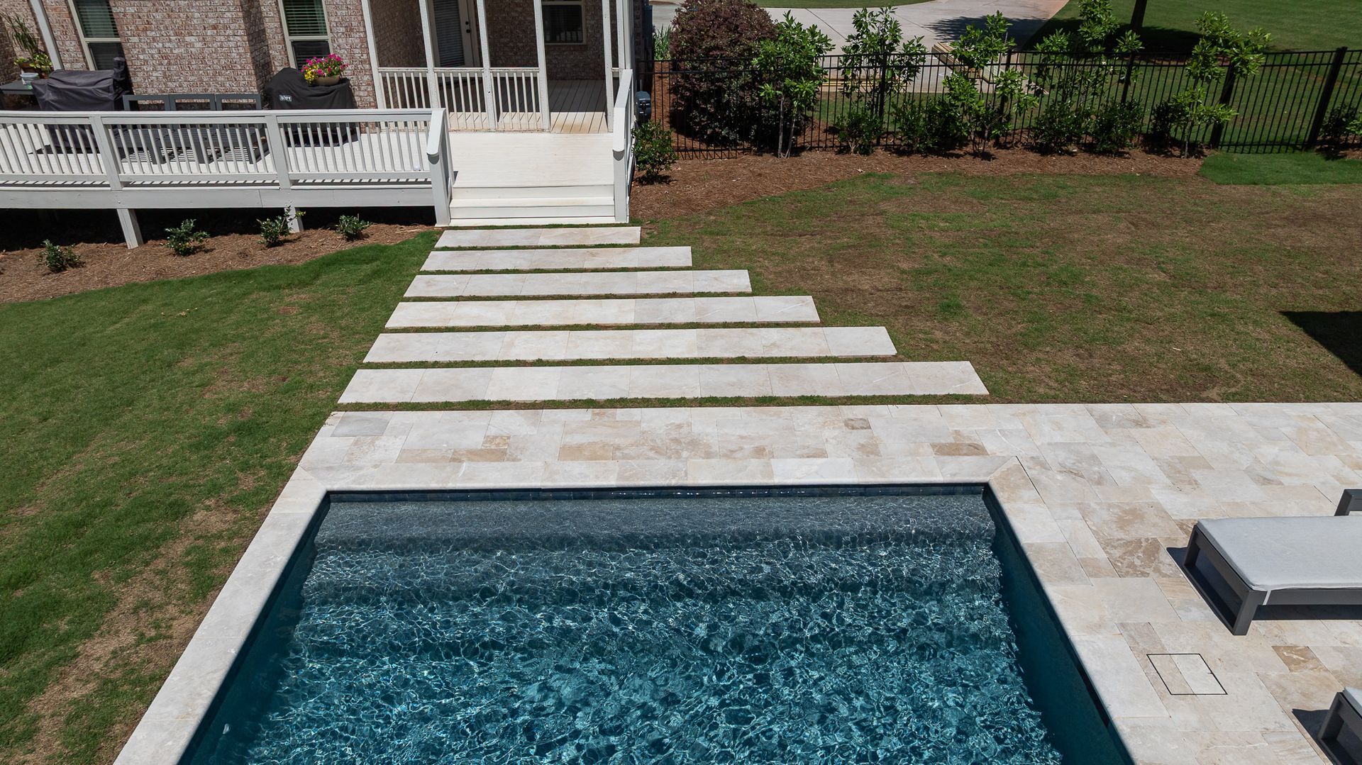Backyard pool with a stone walkway leading to a porch and lawn beyond