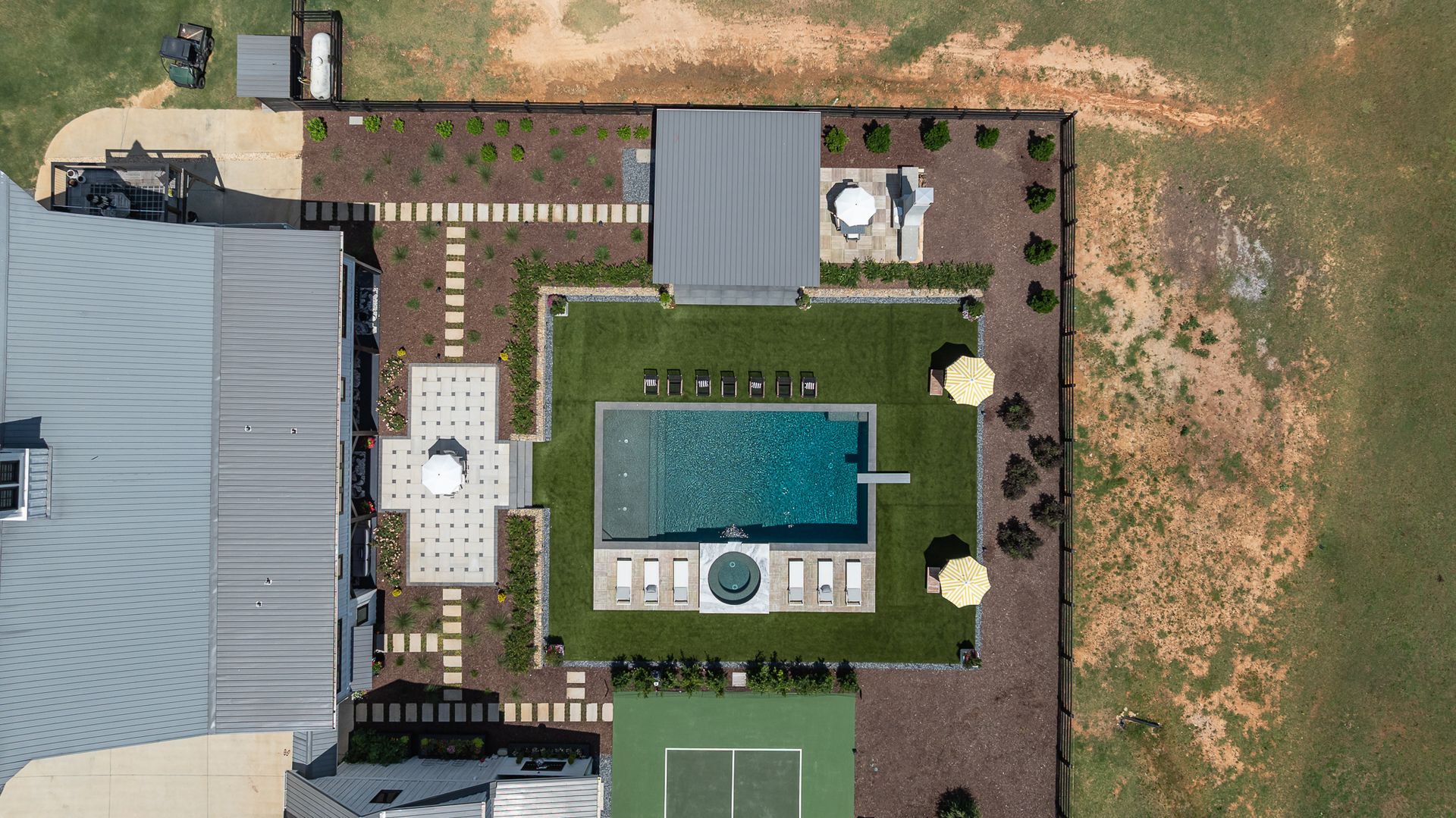 Aerial view of a backyard with a pool, patio, lawn, and adjacent house roof.