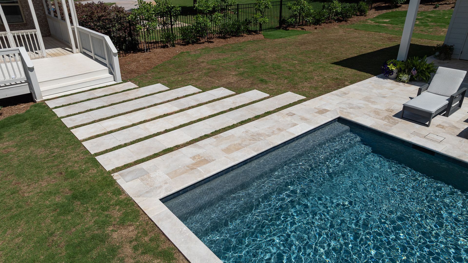 Backyard pool with stone pavers and stepping stones leading to a white deck staircase