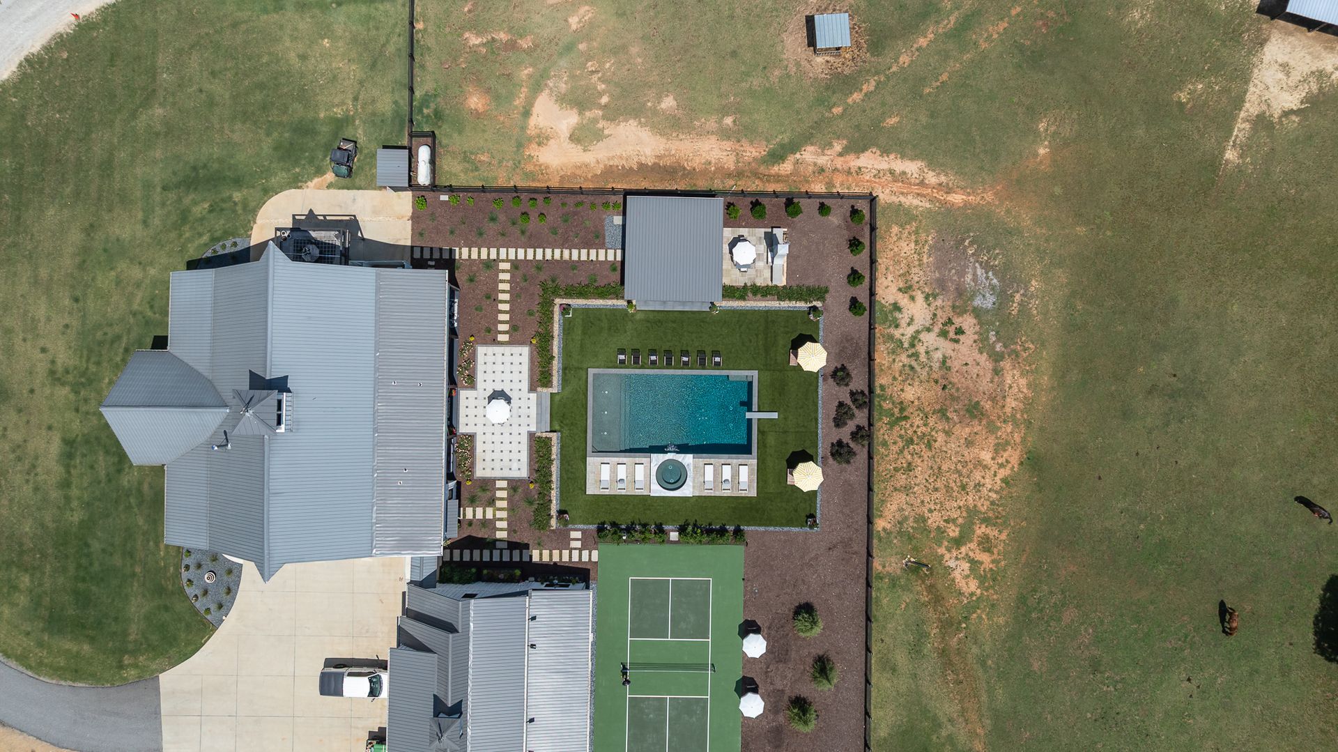 Aerial view of a backyard with a swimming pool, tennis court, patio, and house.
