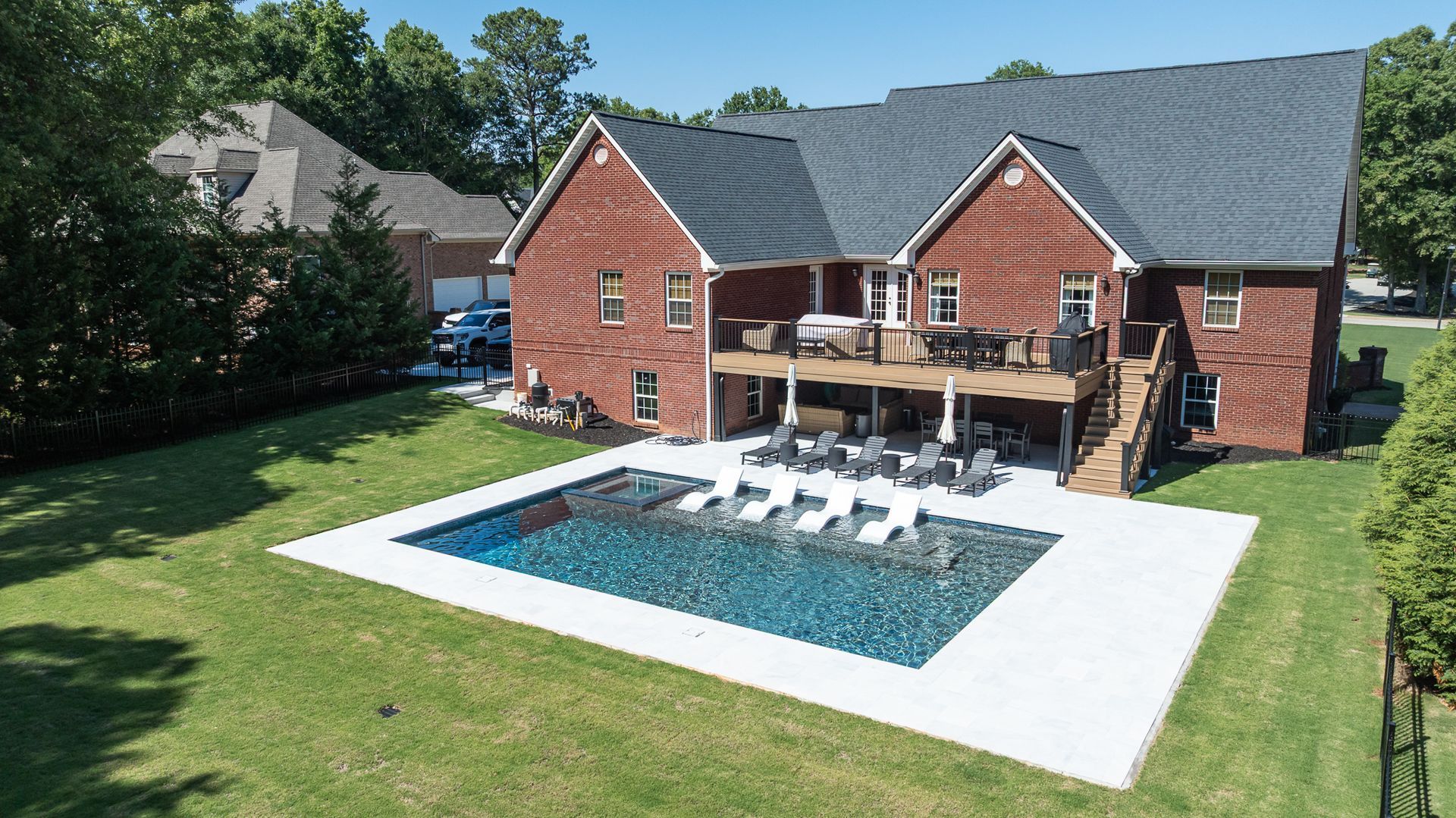 Backyard brick house with a large pool, patio seating, and a manicured lawn