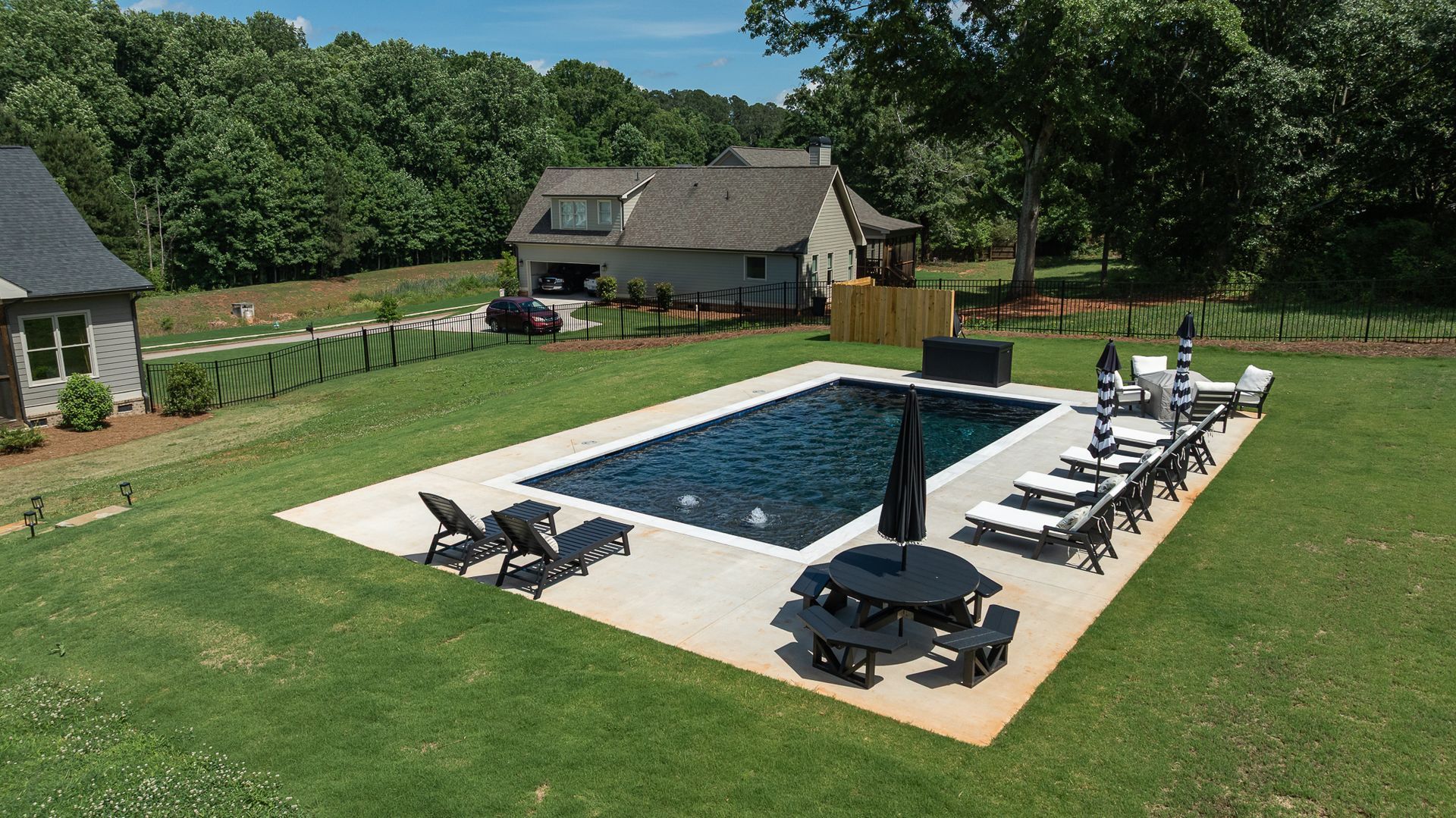 Backyard with rectangular swimming pool, lounge chairs, and a covered grill on a grassy lawn.