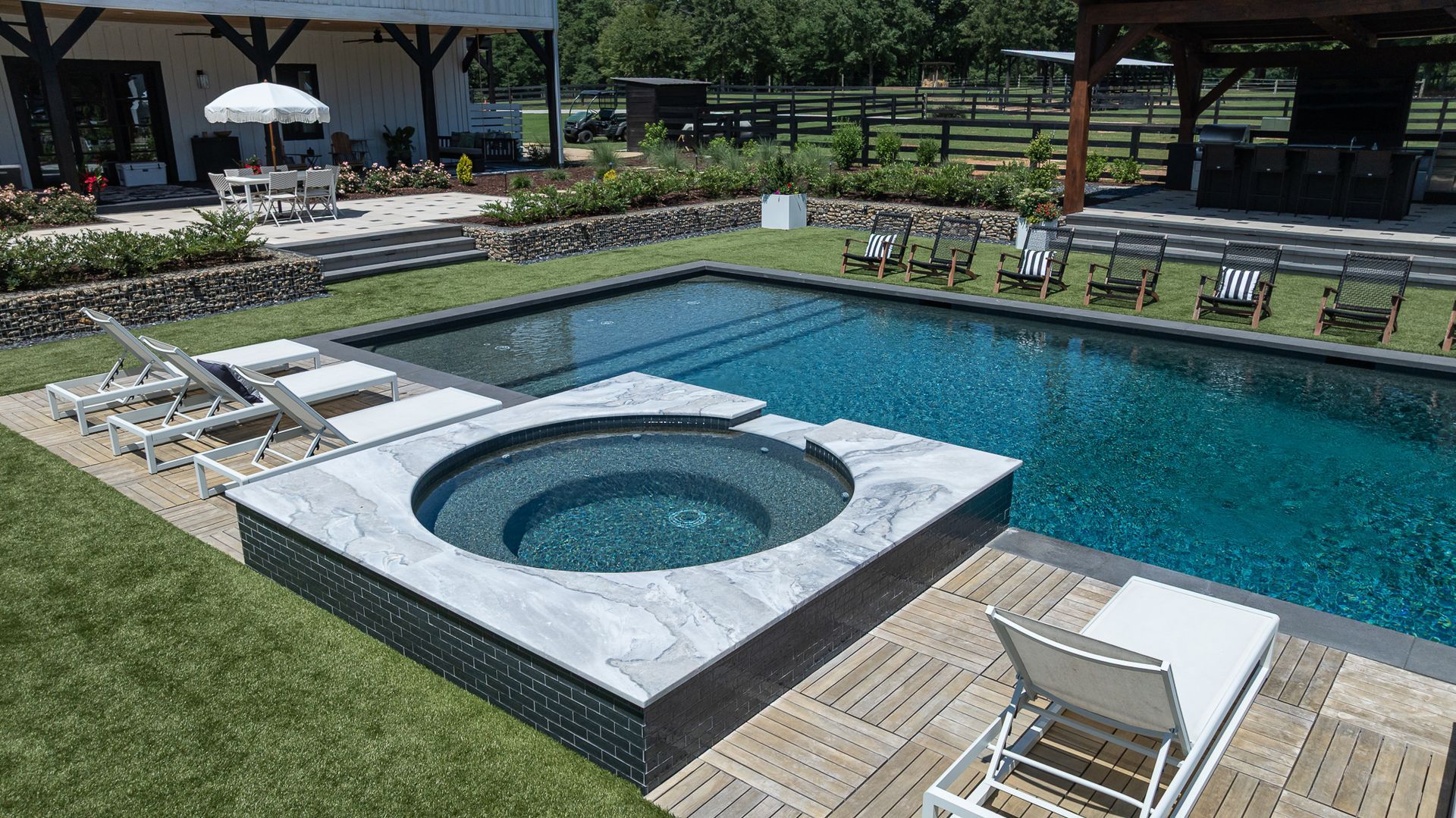 Modern poolside patio with a hot tub, lounge chairs, and lawn by a clear blue pool
