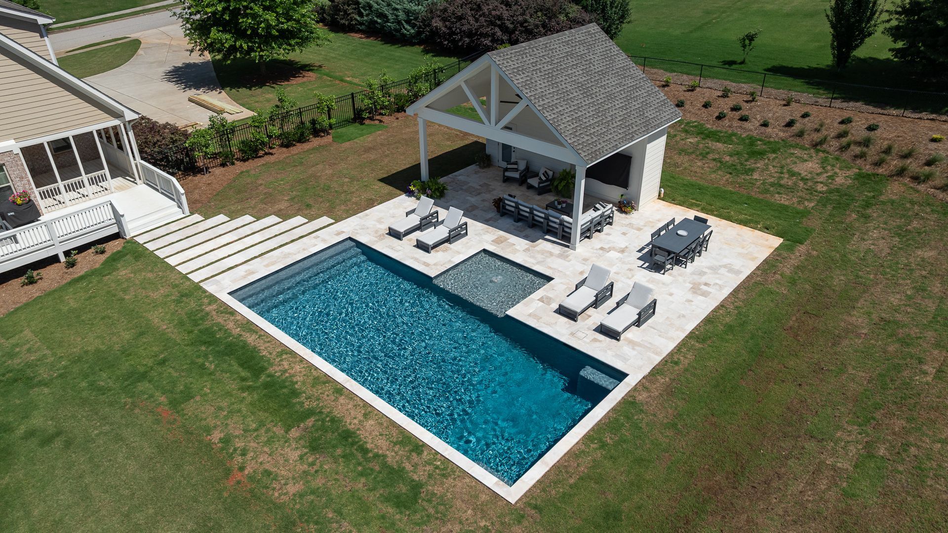 Aerial view of a backyard pool with a pavilion, lounge chairs, and a small dining area on a patio.