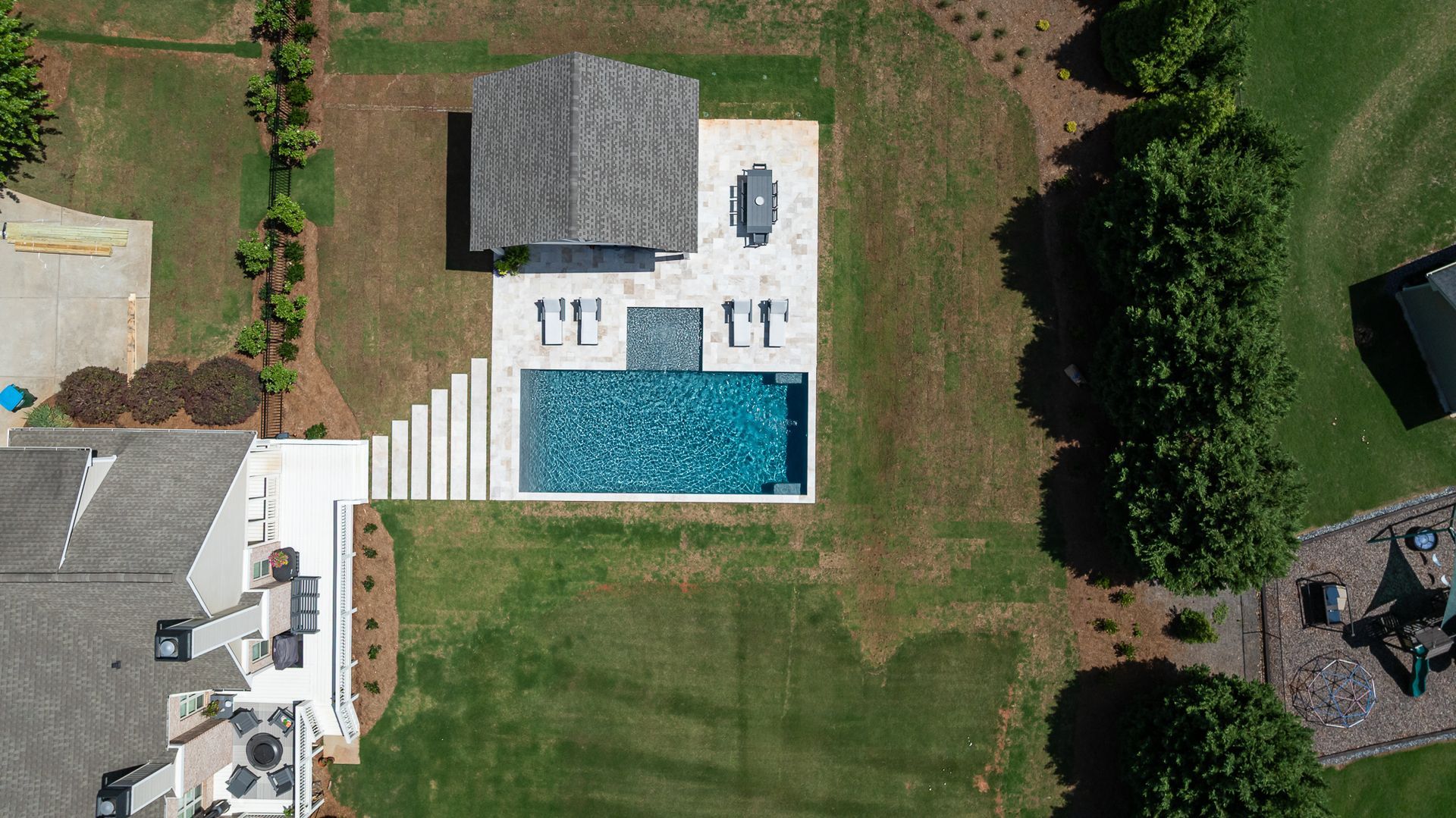 Aerial view of a backyard pool, patio, and lawn beside a house and small outbuilding.