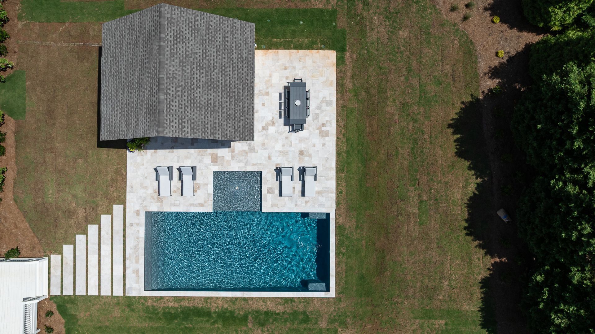 Aerial view of a backyard pool patio with lounge chairs, a hot tub, and a small covered structure.