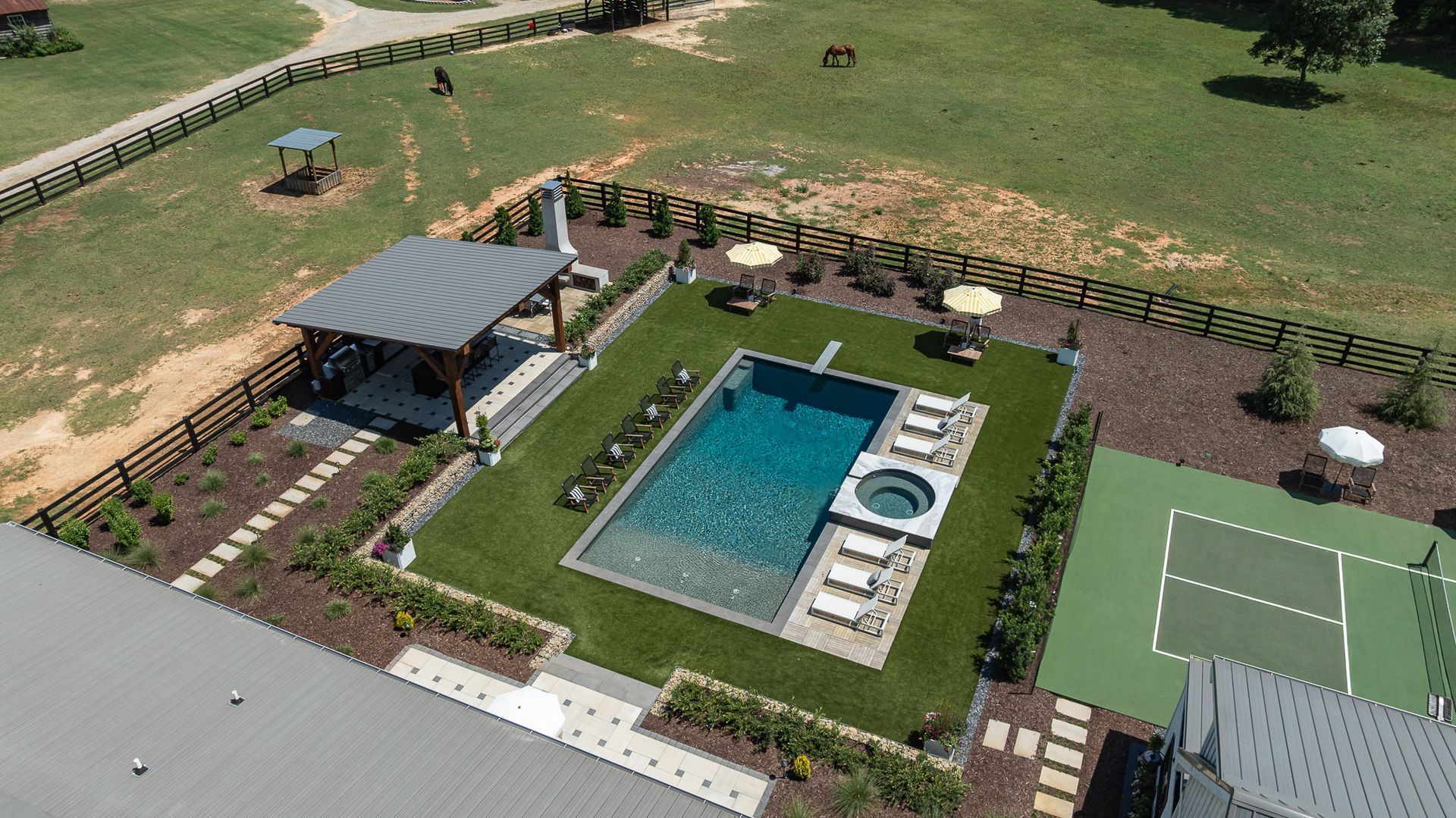 Aerial view of a backyard with a swimming pool, lounge chairs, pergola, and tennis court.