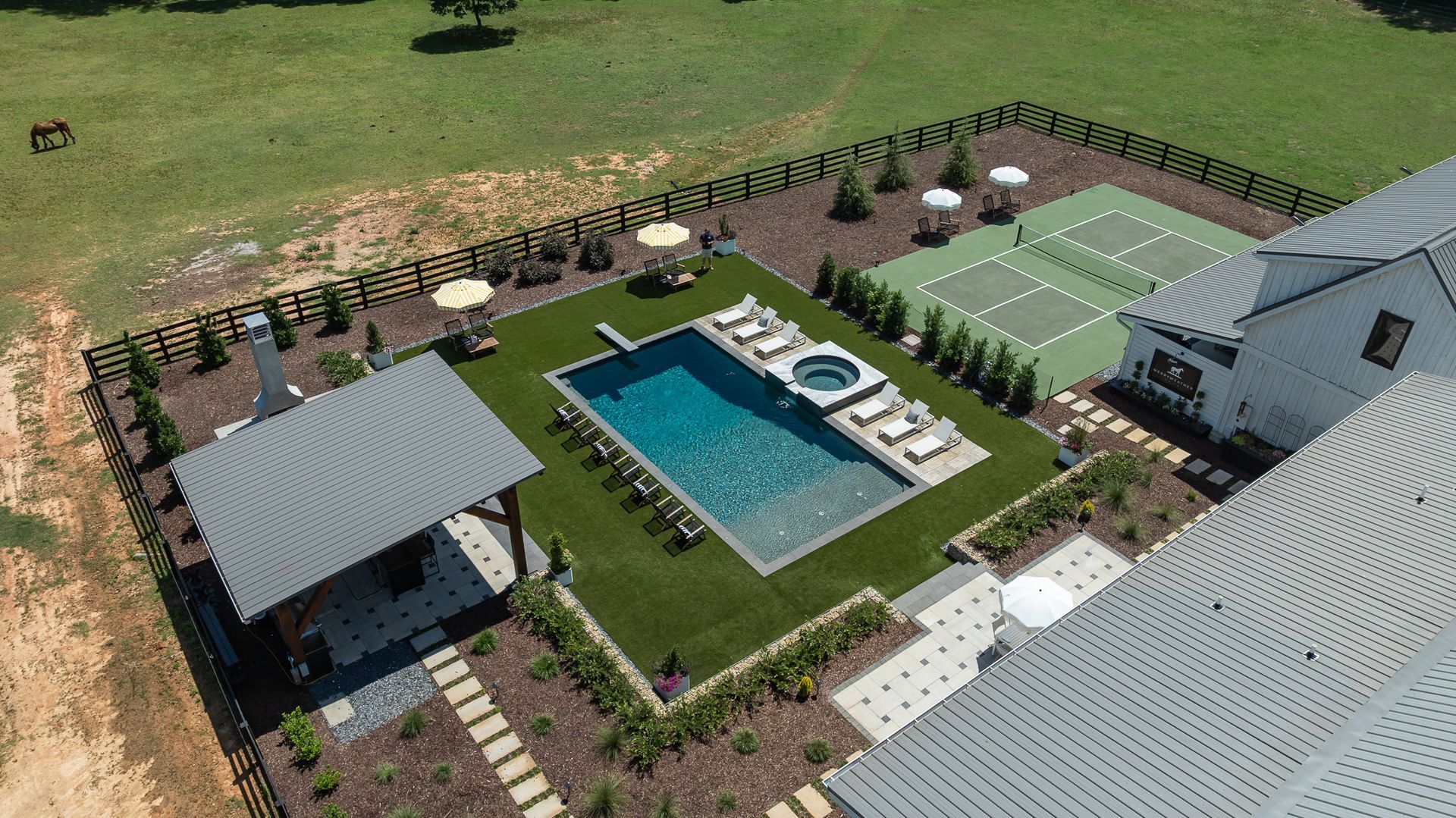Aerial view of a backyard with pool, hot tub, tennis court, lounge chairs, and a covered patio.