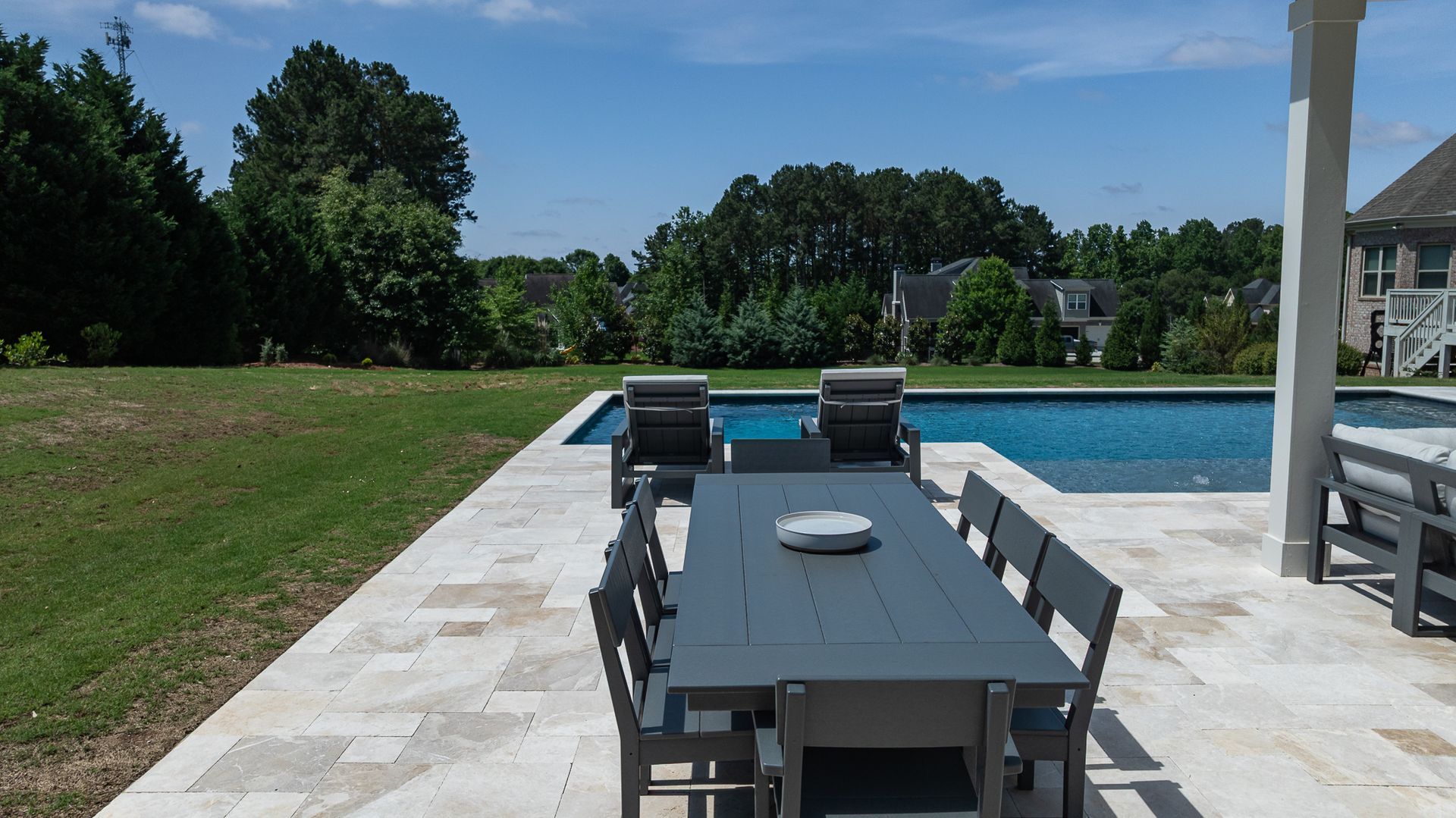 Patio dining table beside a backyard swimming pool under a sunny sky
