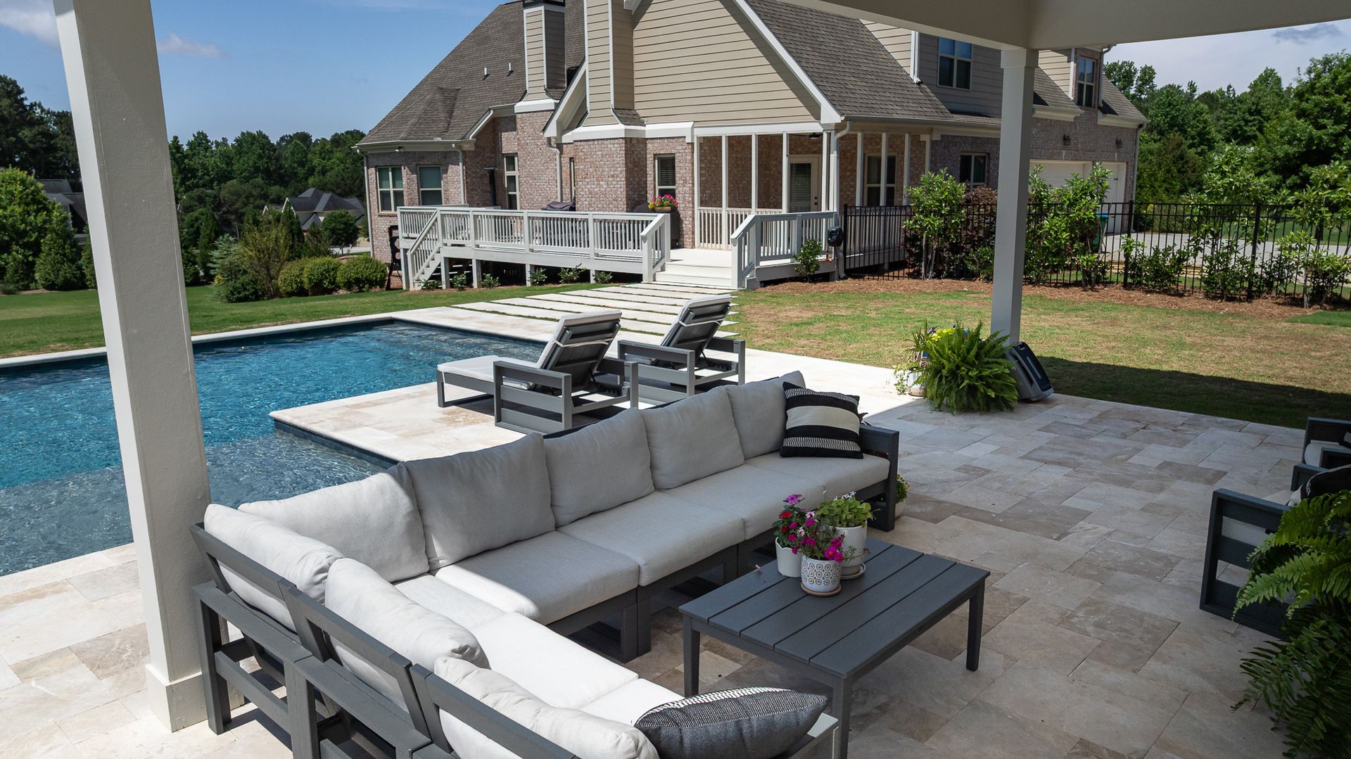 Poolside patio with white sectional seating, lounge chairs, and a house in the background