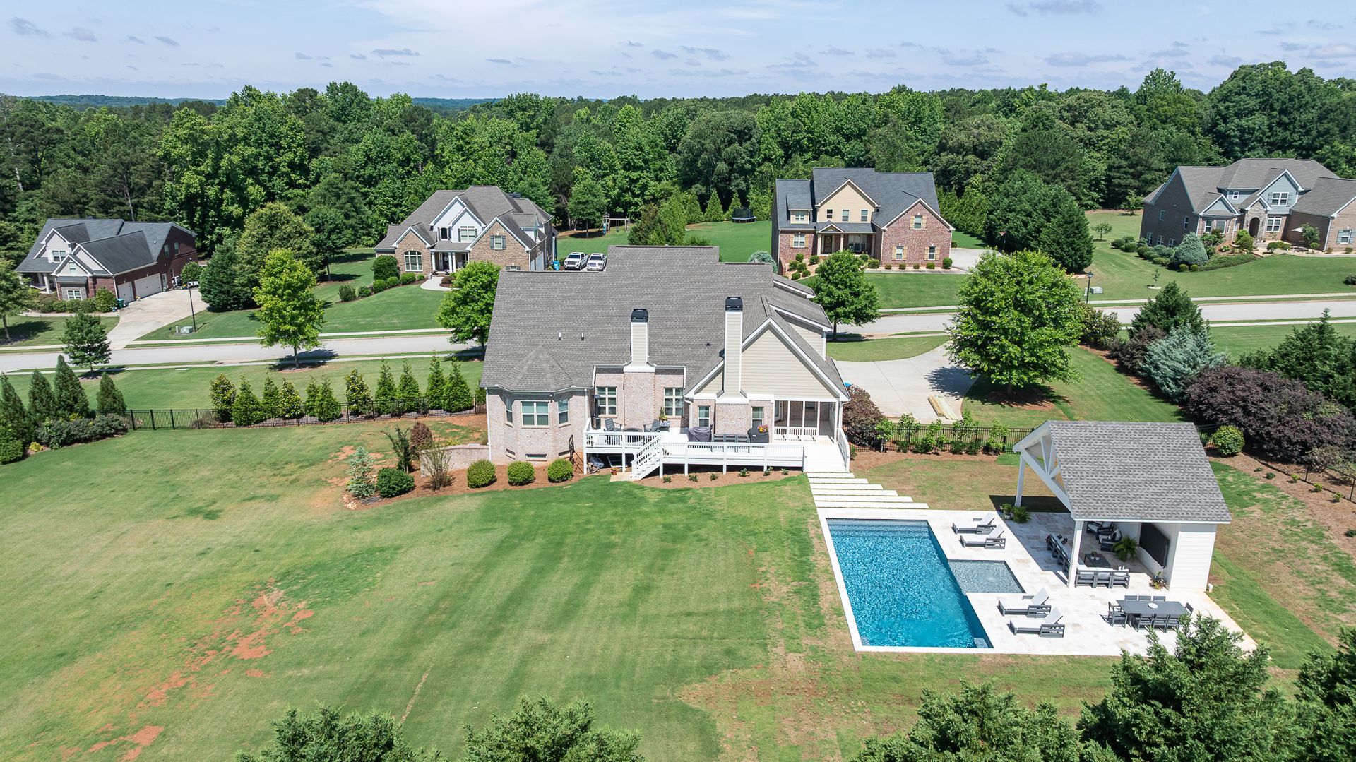 Aerial view of a large suburban home with a pool, patio, and surrounding houses and trees