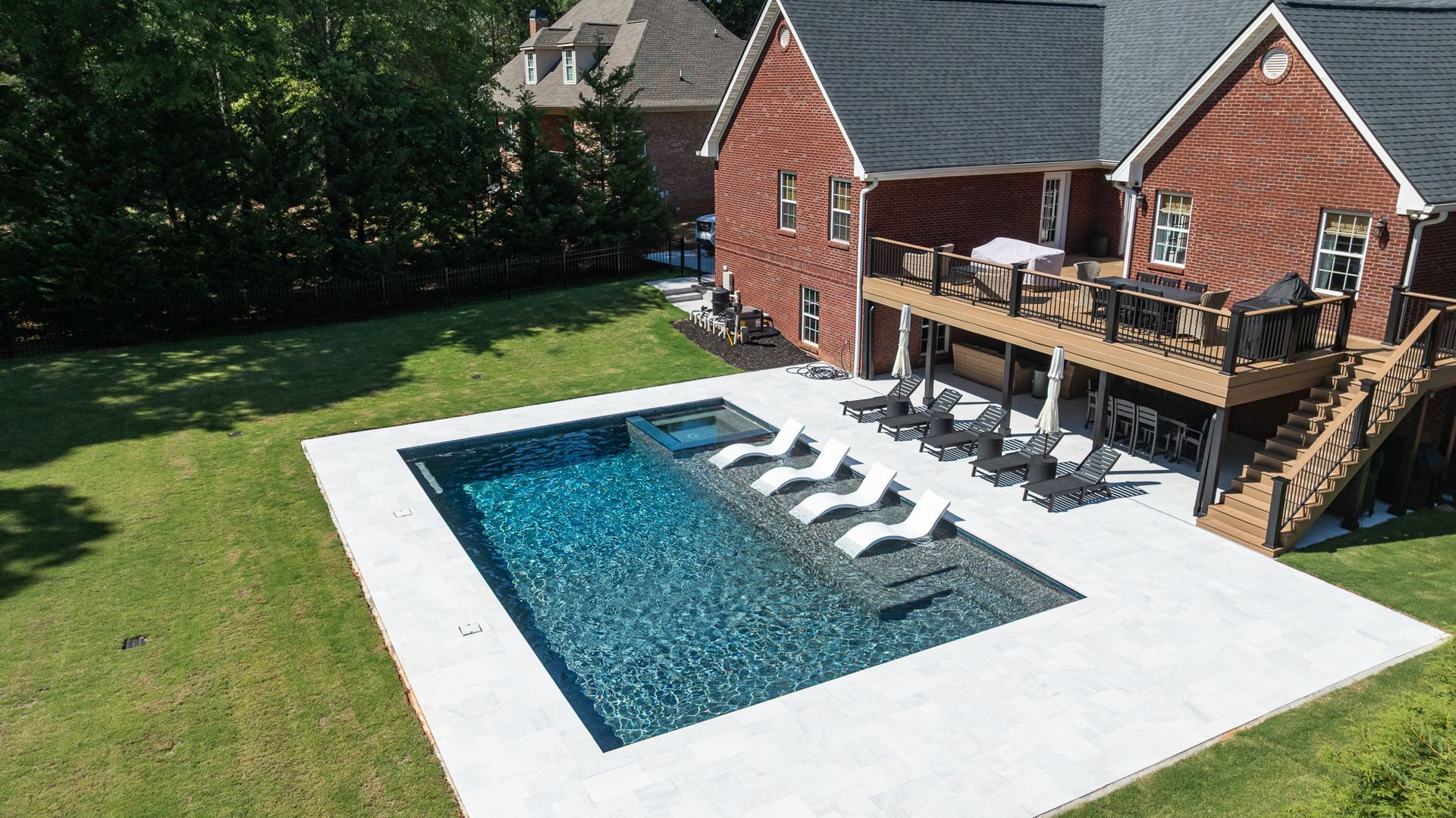 Backyard swimming pool beside a brick house with lounge chairs and a wooden deck