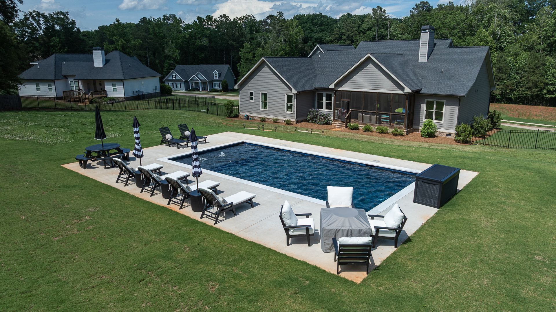 Backyard with a rectangular pool, lounge chairs, and a patio beside a large house