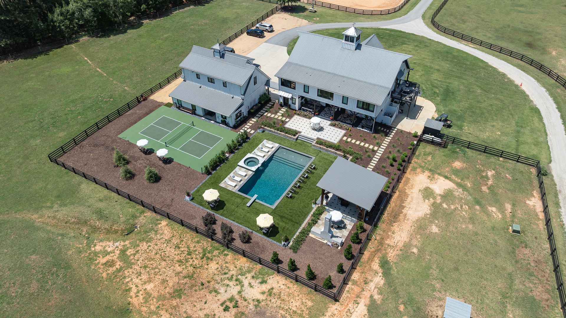 Aerial view of a modern house with a backyard pool, patio, and landscaped lawn surrounded by open fields