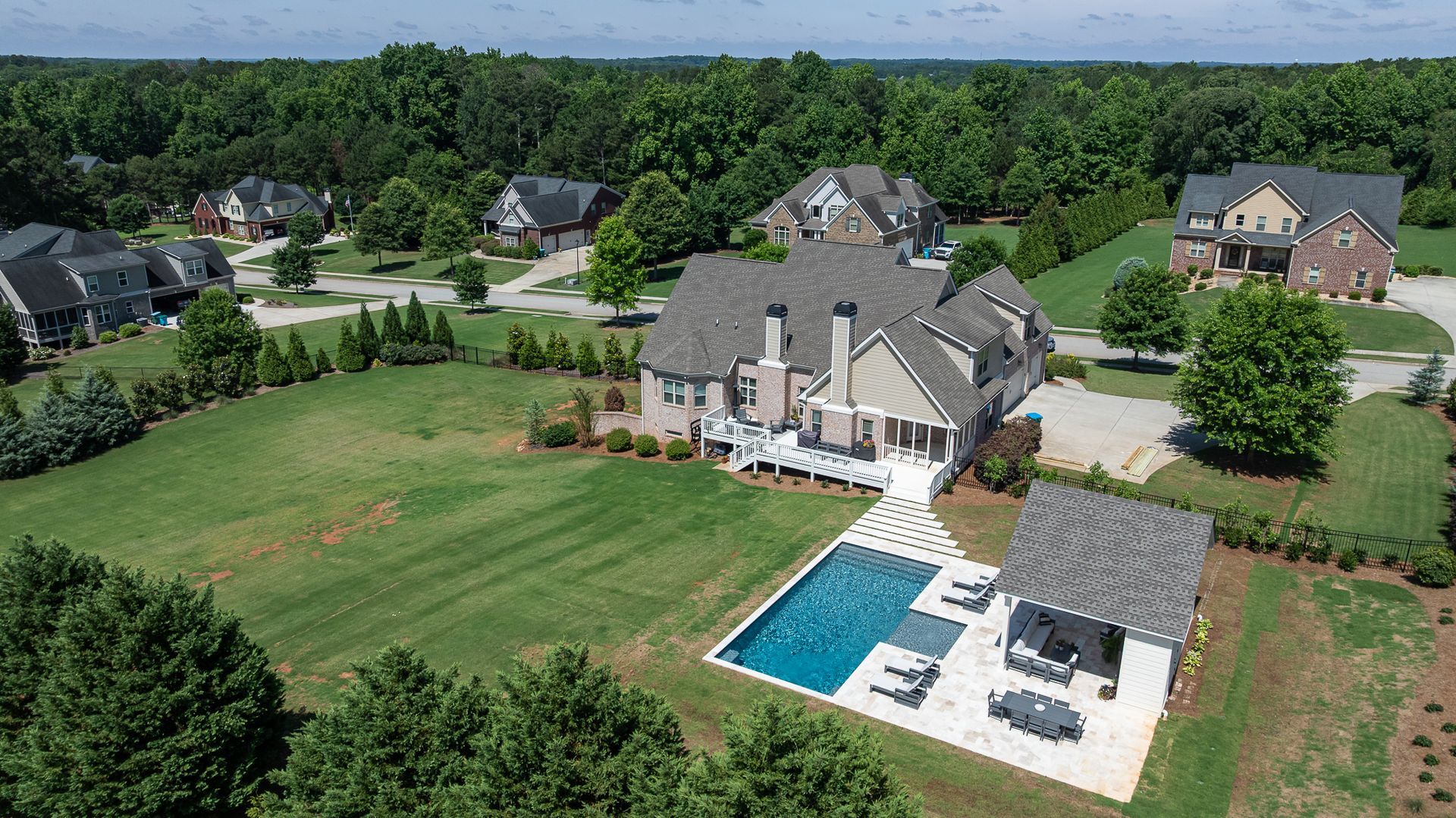 Aerial view of a large suburban house with a backyard pool, patio, and wide green lawn