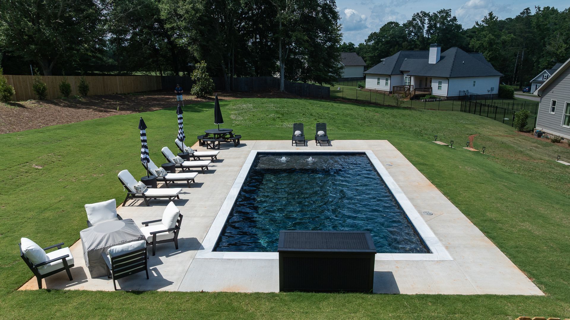 Backyard pool with lounge chairs, umbrellas, and a white deck in a grassy suburban yard.