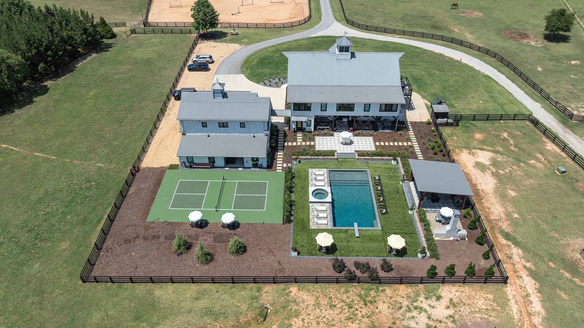 Aerial view of a large modern house with pool, tennis court, patio, and landscaped backyard