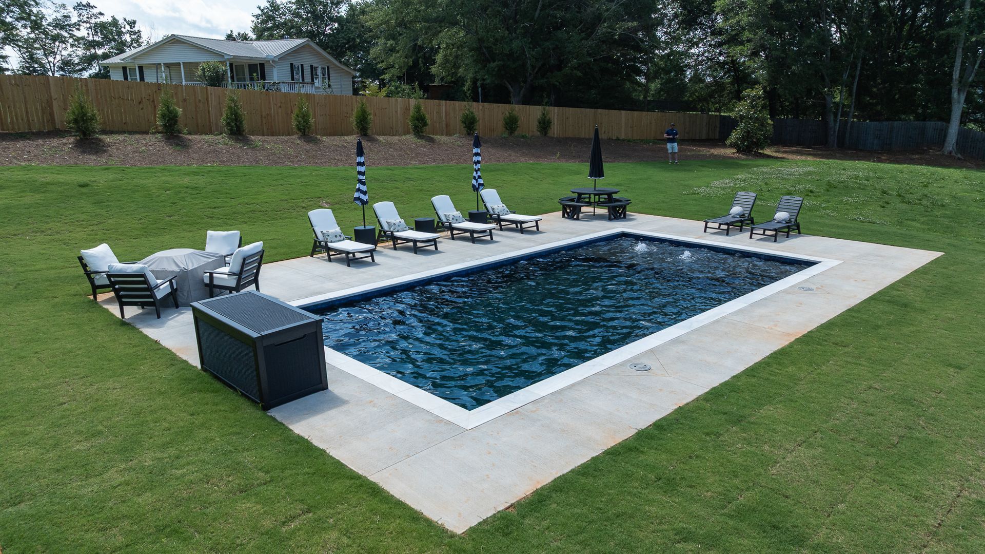 Backyard pool with lounge chairs, umbrellas, and a patio beside a grassy lawn