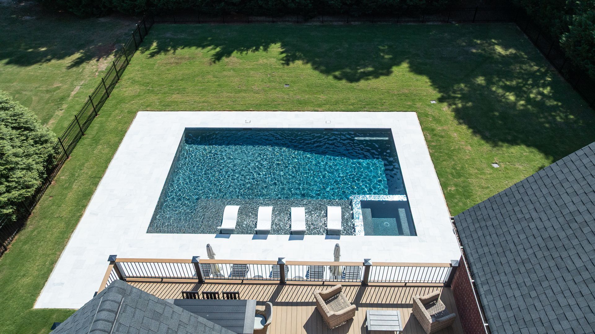 Backyard swimming pool with a white deck, turquoise water, and lounge chairs beside a grassy lawn