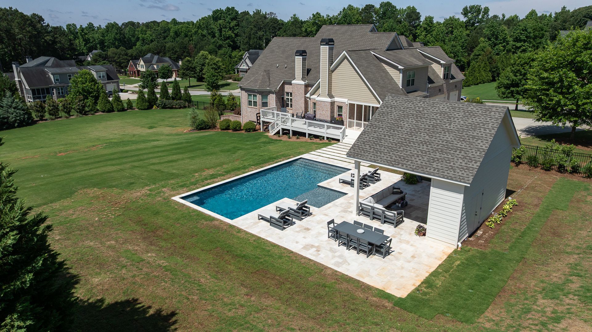 Aerial view of a large suburban home with a backyard pool, patio, and expansive green lawn
