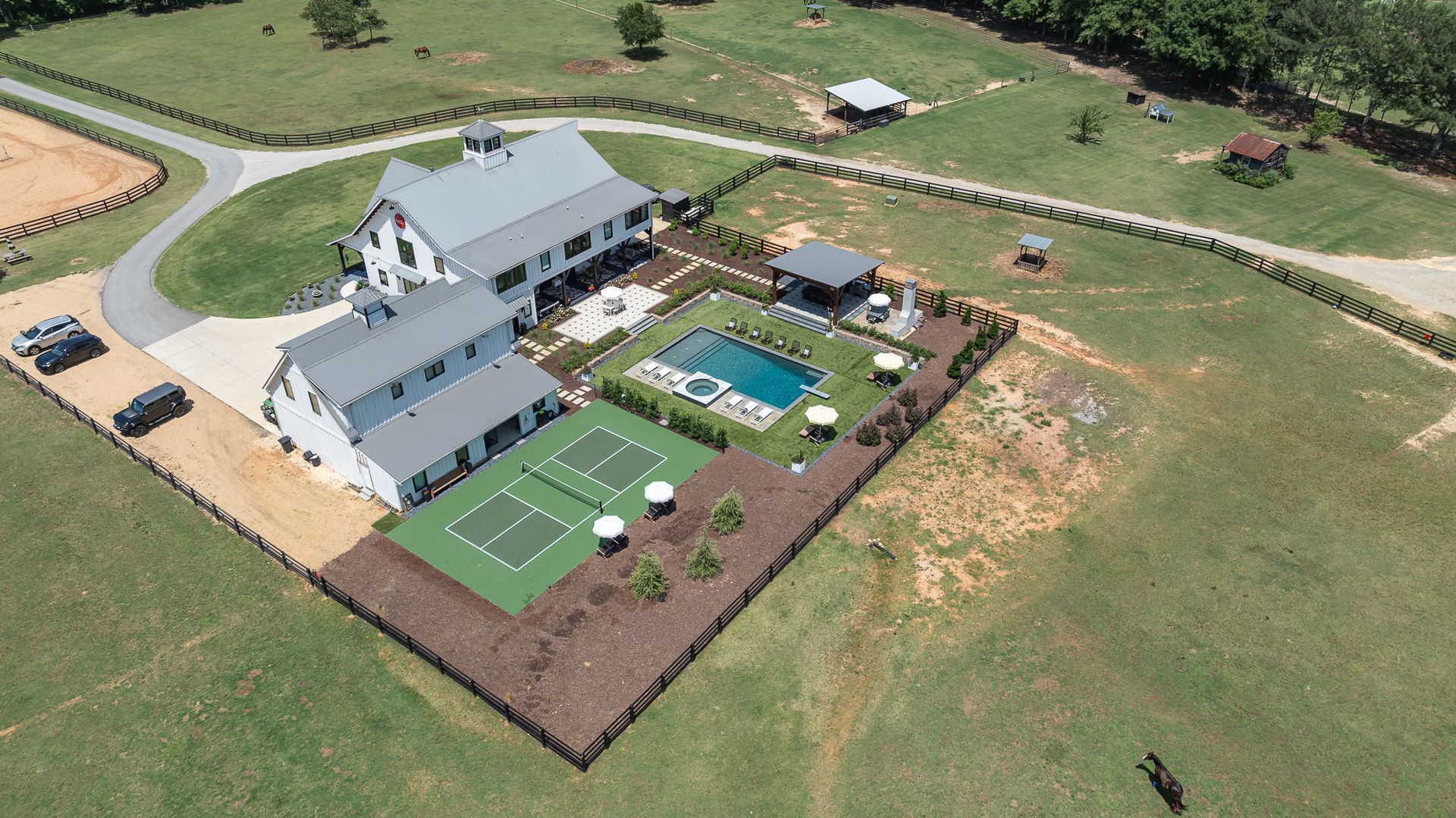 Aerial view of a house with a fenced backyard, patio, green lawn, and pool on open farmland