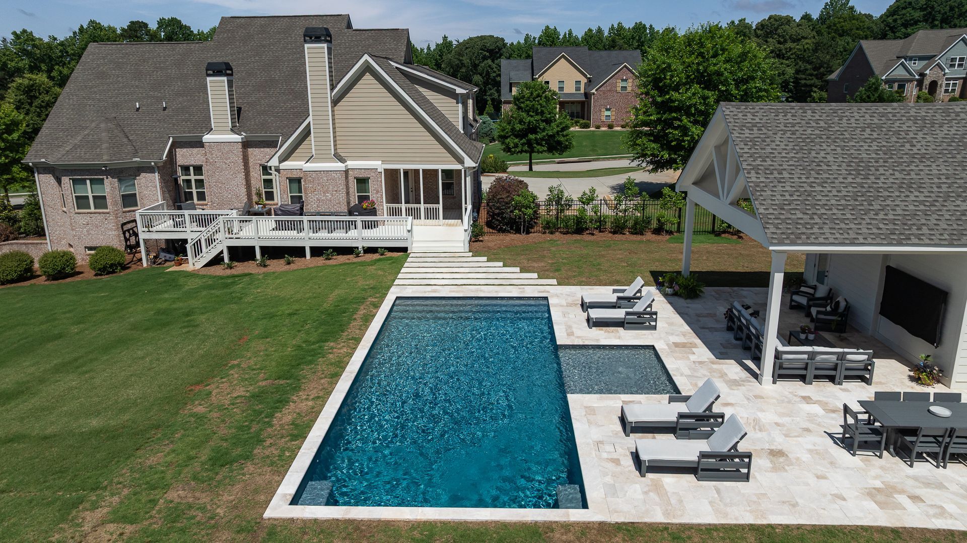 Backyard with rectangular pool, white stone patio, lounge chairs, and a covered outdoor seating area beside a house